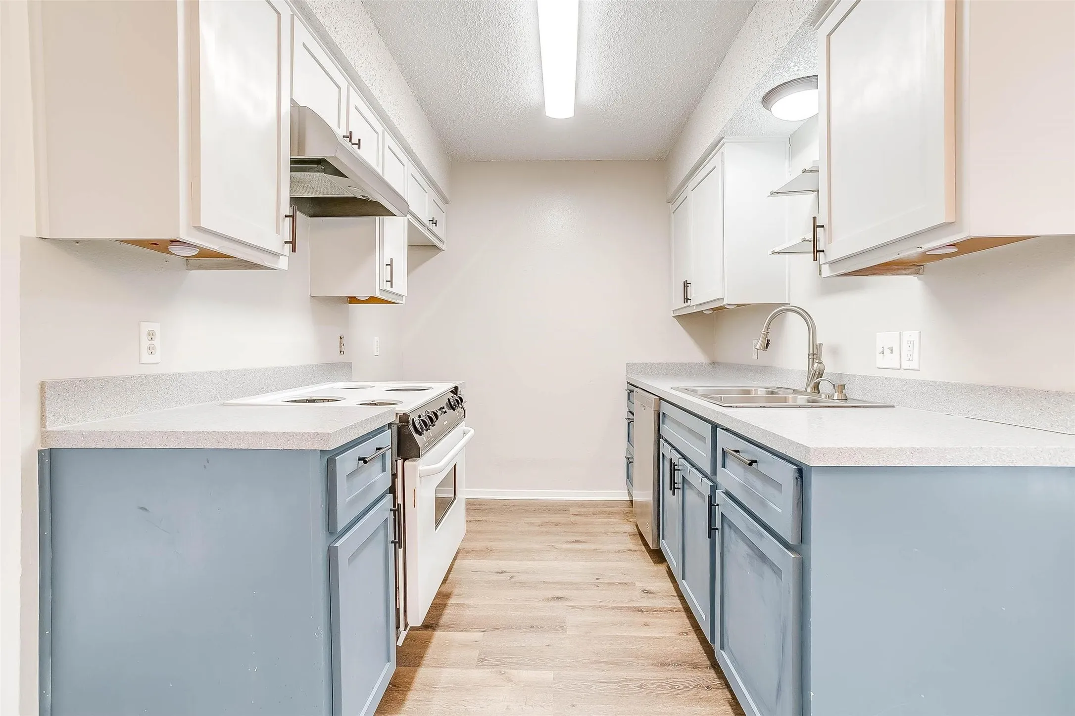 Galley kitchen featuring light-colored countertops, dual-toned cabinetry, light wood-finish flooring, and a stainless steel sink with a gooseneck faucet