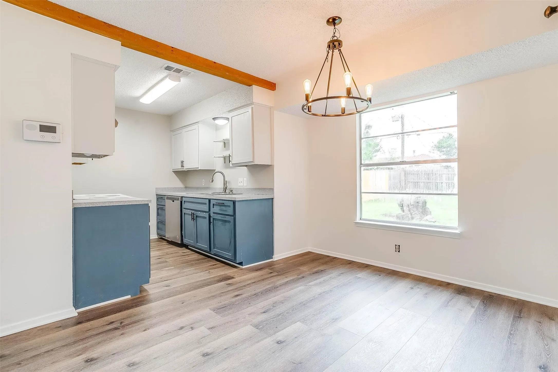 Open-concept space featuring wood-finish flooring, a kitchen with two-tone cabinetry, and a window providing natural light