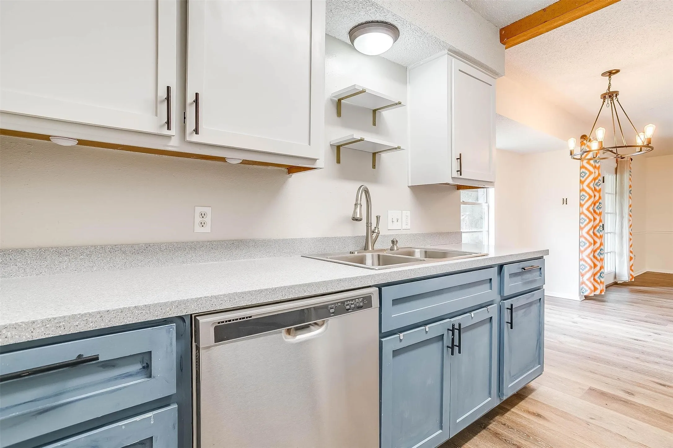Two-tone kitchen cabinetry, stainless steel sink with gooseneck faucet, light-toned countertops, stainless steel dishwasher, and wood-finish flooring
