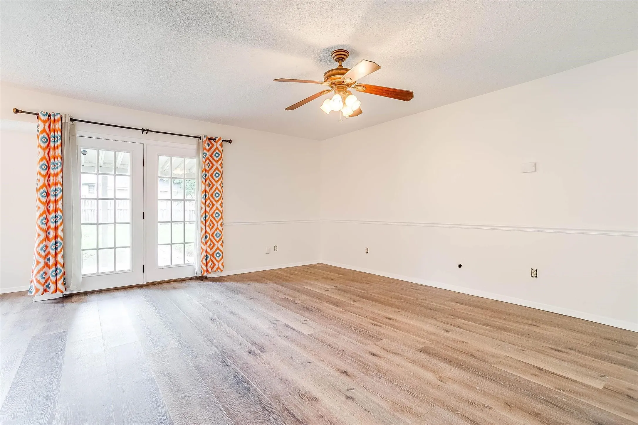 Wood-finish flooring, white walls with chair rail molding, and a ceiling fan with light fixture