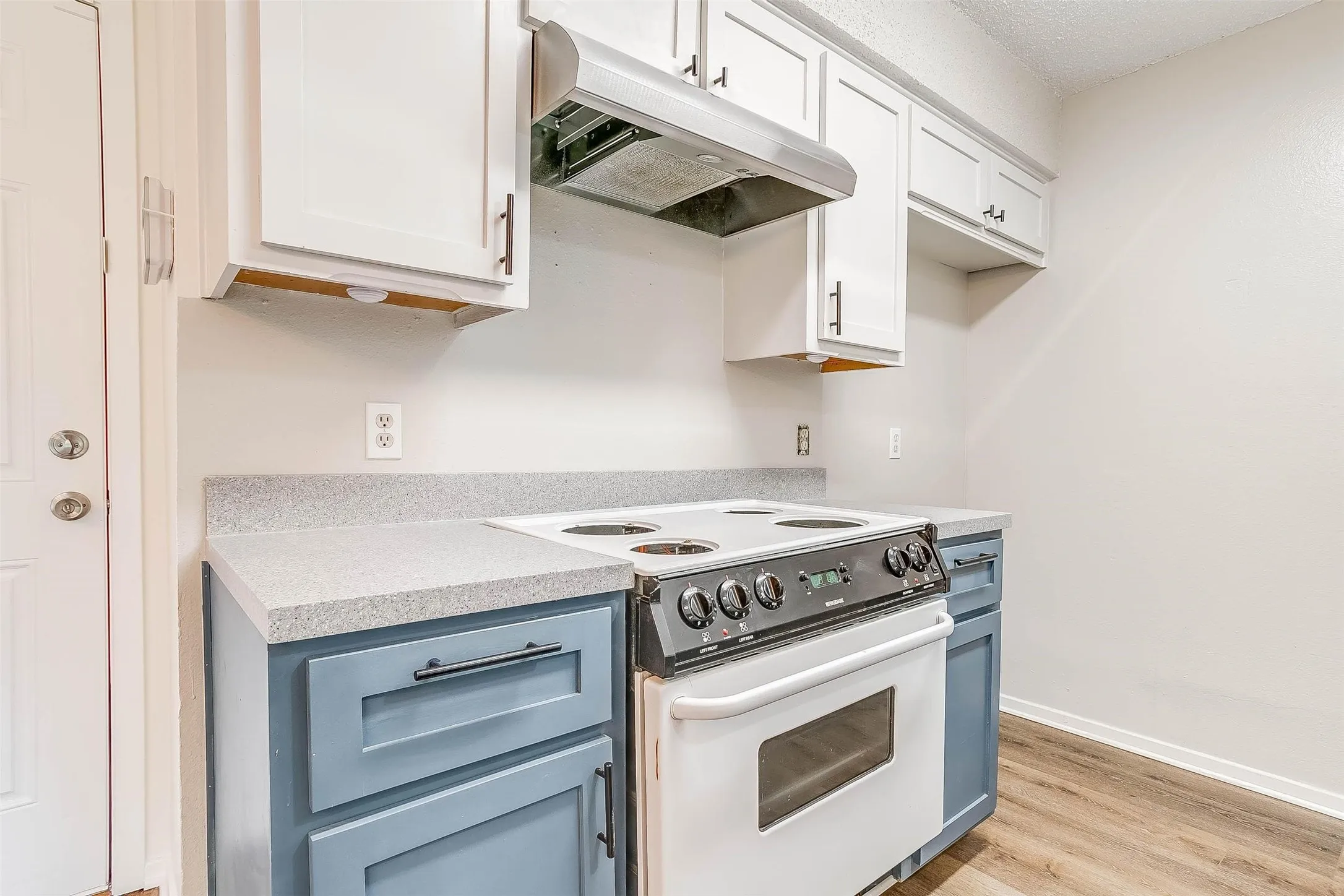 White upper cabinetry, blue lower cabinetry, composite countertops, wood-finish flooring, and a stainless steel range hood