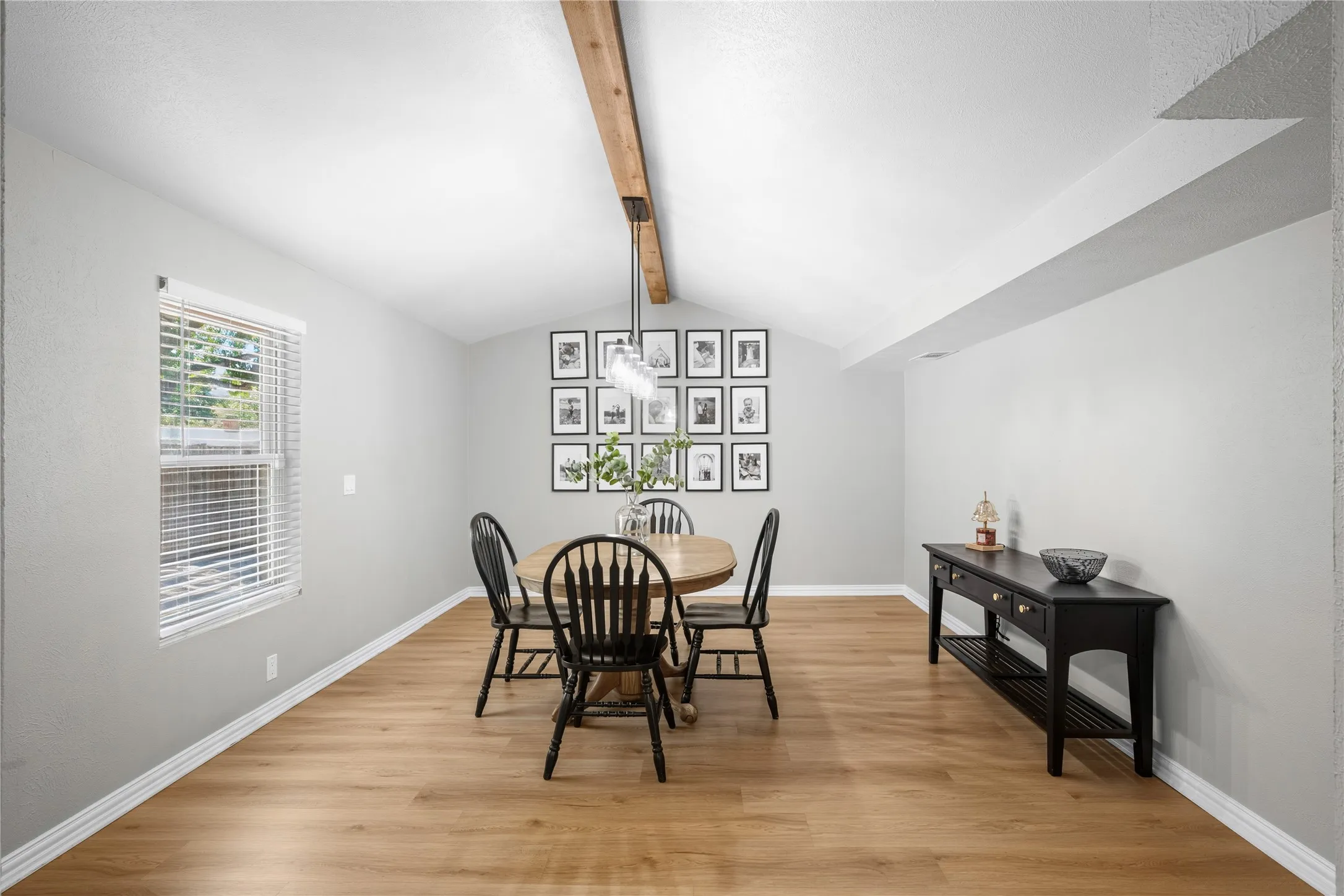 Vaulted ceiling with exposed wood beam, wood-finish flooring, neutral wall paint, and natural light from a double-hung window