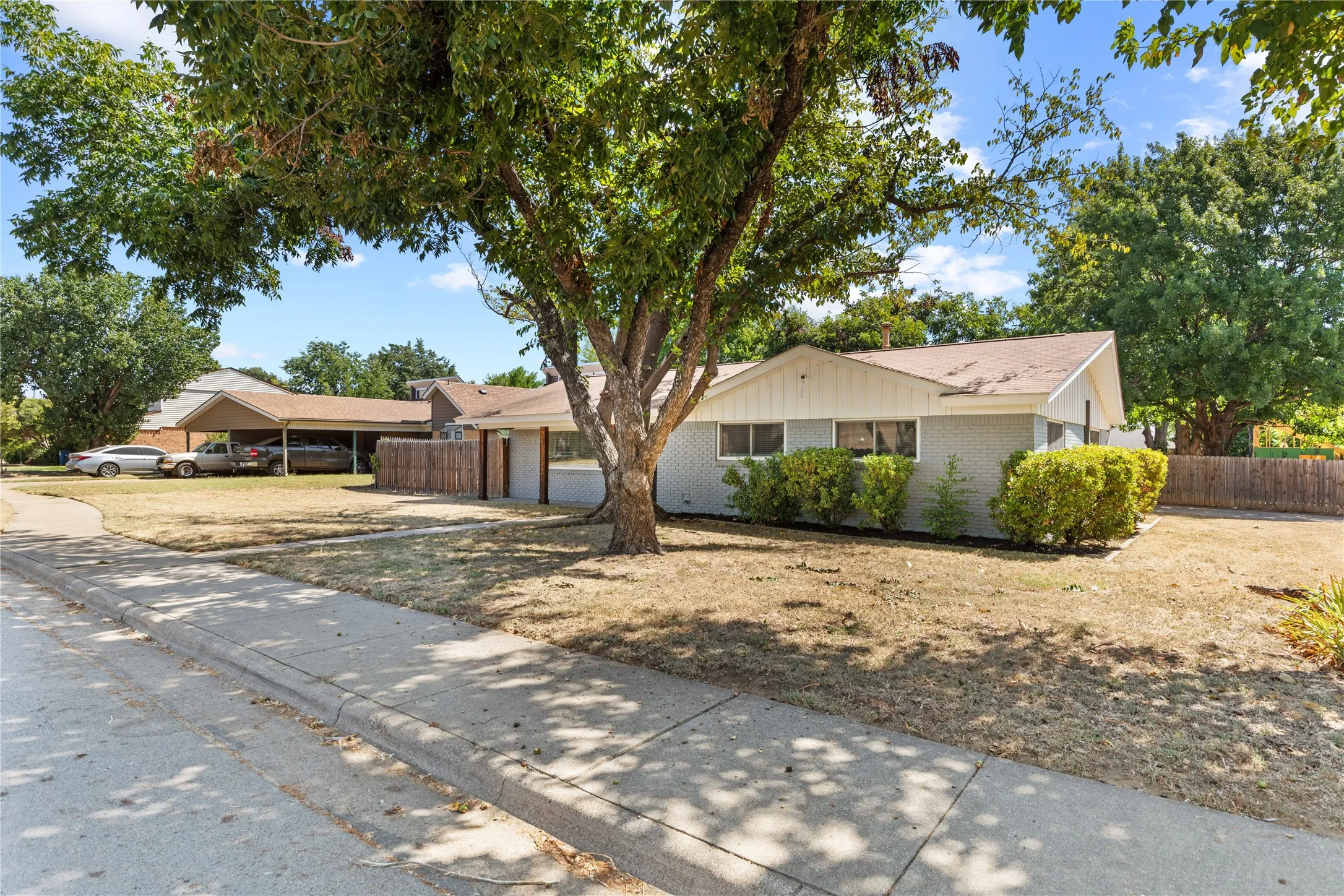 Single-story residence with a gray exterior, white trim, and a prominent mature tree in the front yard