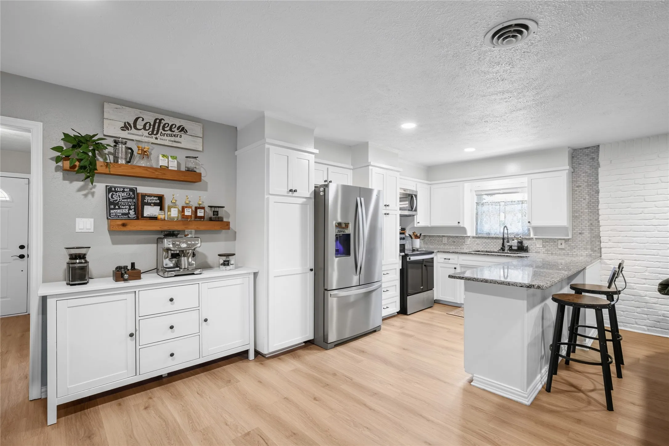Kitchen featuring wood-finish flooring, white cabinetry, stainless steel appliances, a breakfast bar, and a textured brick accent wall