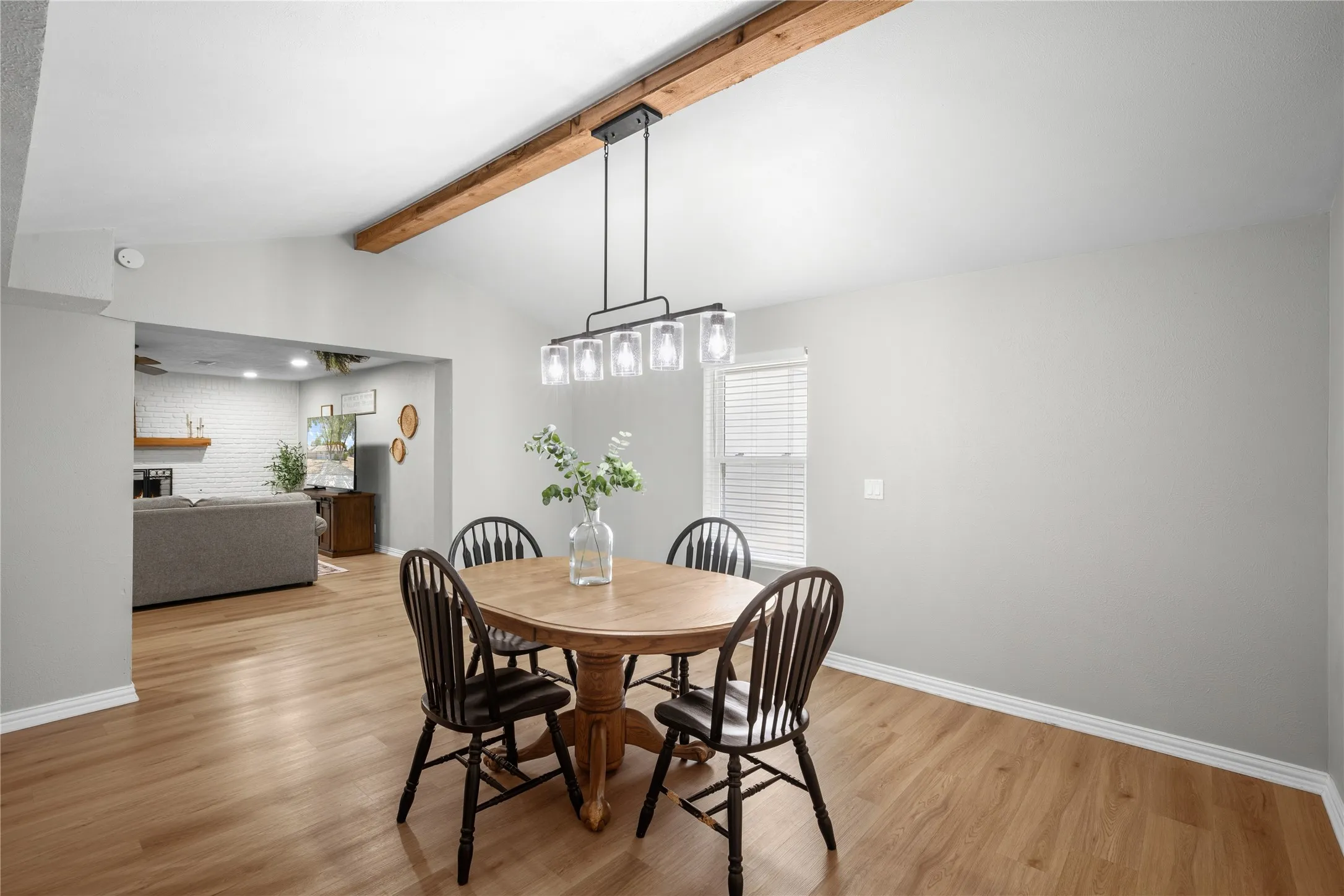 Vaulted ceiling with exposed wood beam, wood-finish flooring, and a linear chandelier with clear glass shades