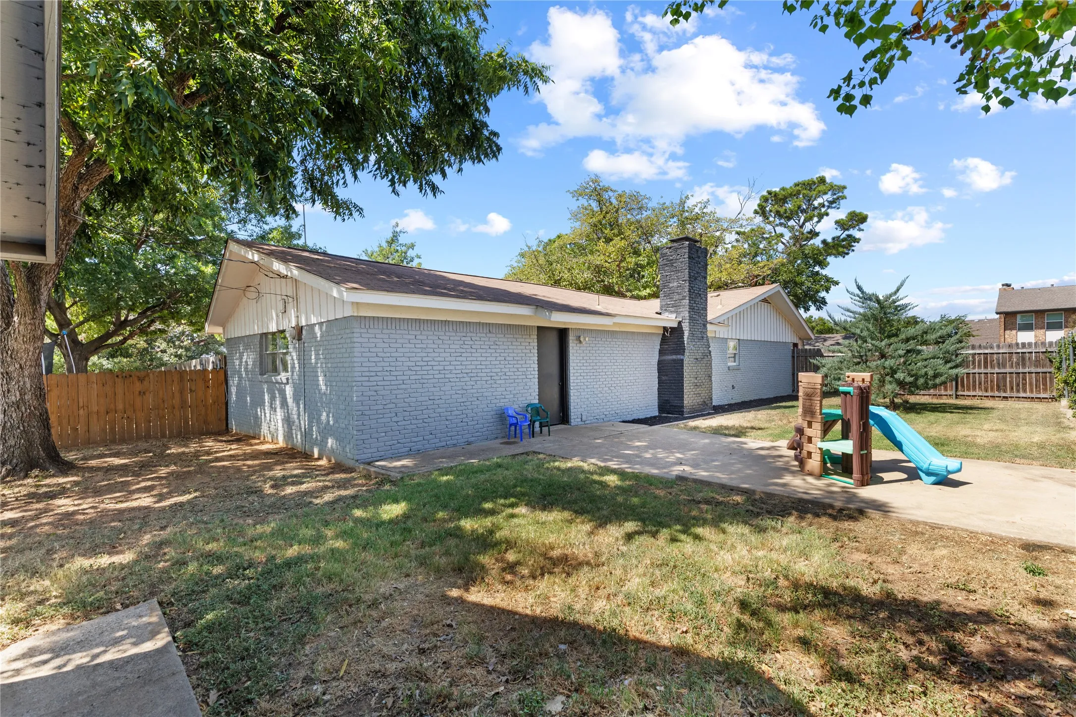 Expansive backyard with a concrete patio, wood fence, and mature trees