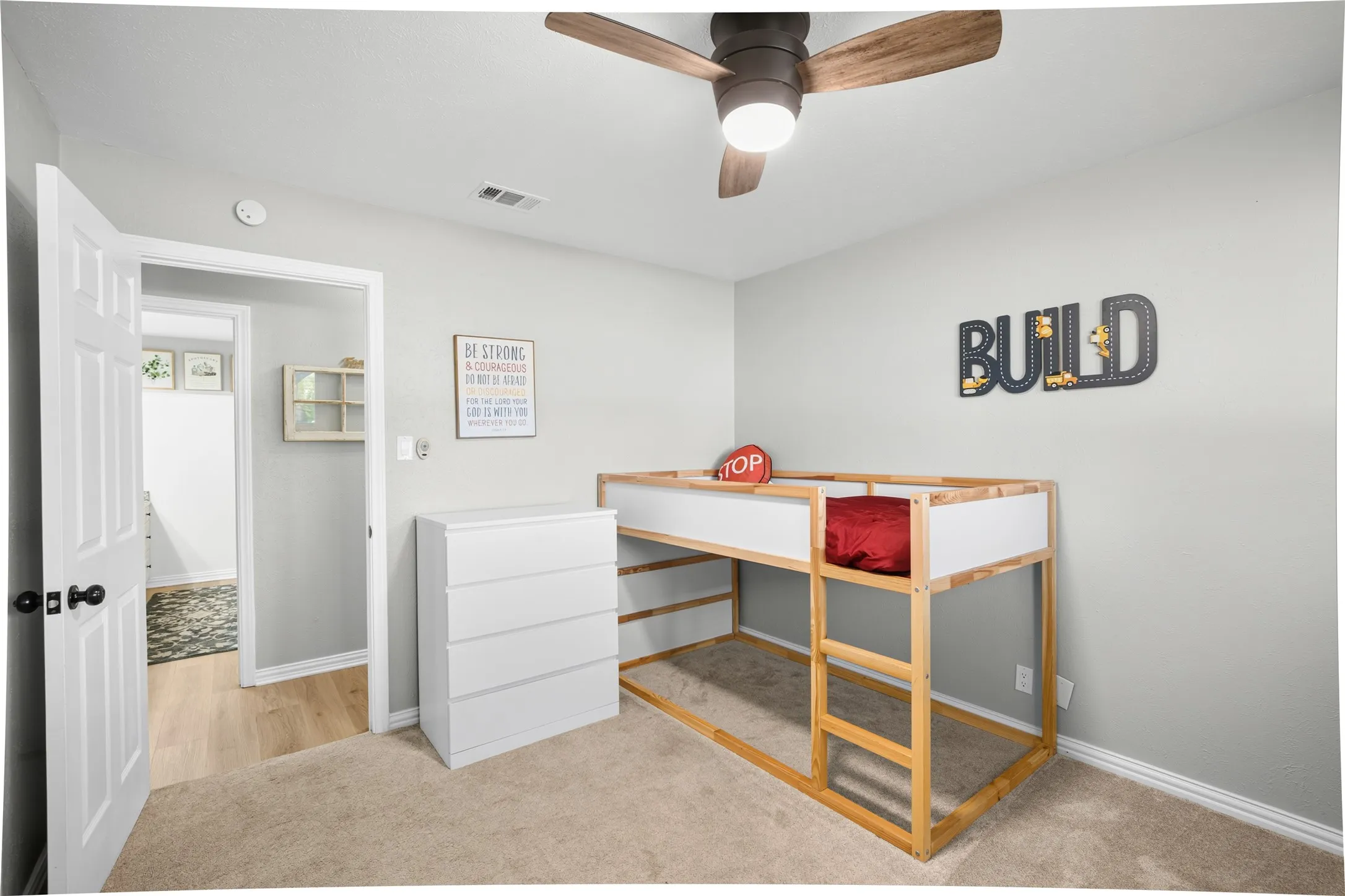 Neutral wall paint, ceiling fan with wood-finish blades, and carpeted flooring
