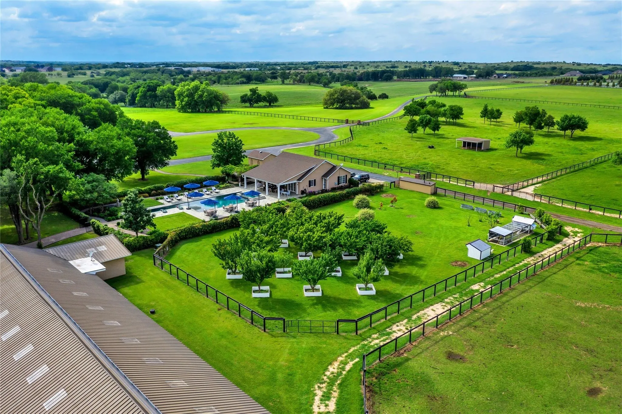 Expansive green grounds with manicured lawns, a large main residence, a swimming pool with lounge areas, an additional outbuilding, and fenced perimeters
