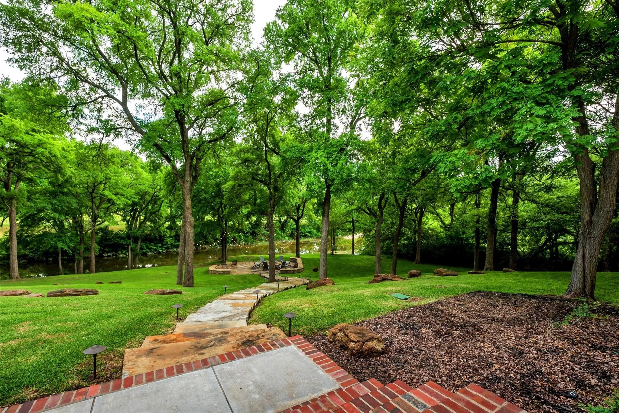Expansive backyard featuring a manicured lawn, mature trees, and a winding stone pathway
