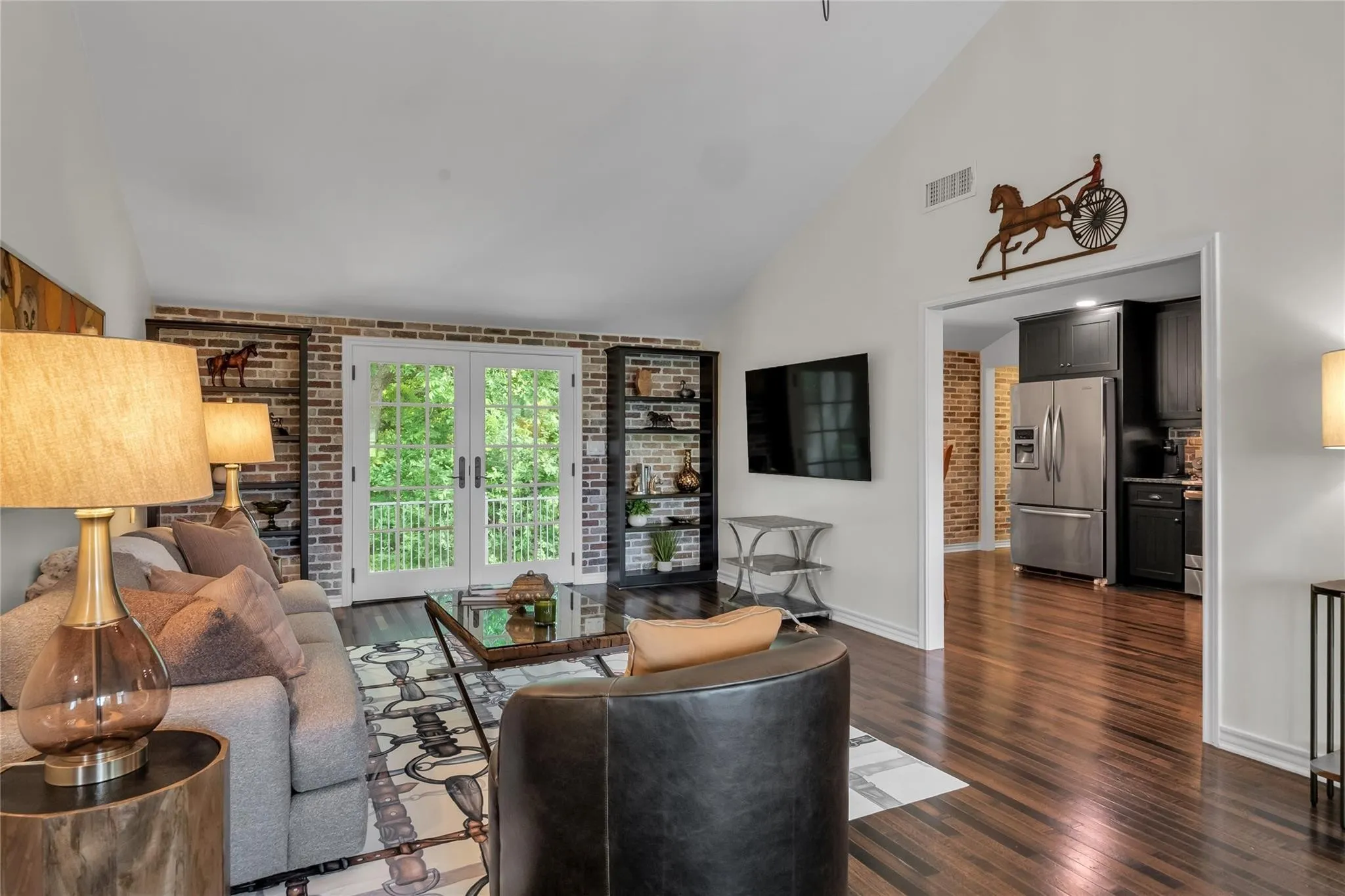 Vaulted ceiling, dark wood-finish flooring, French doors, exposed brick accent walls, and stainless steel kitchen appliances