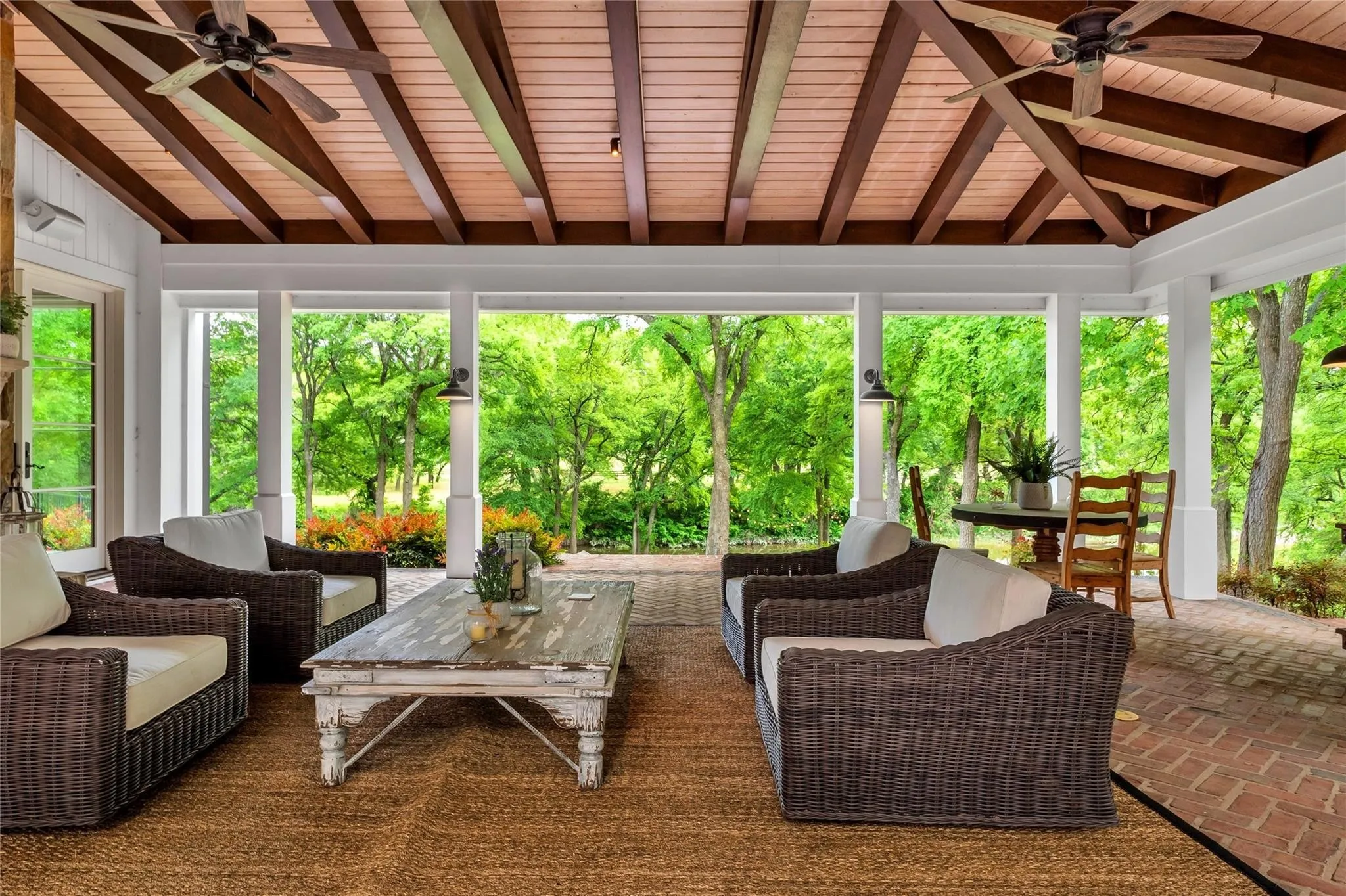 Expansive covered patio featuring a wood-plank ceiling with exposed beams, ceiling fans, and brick flooring