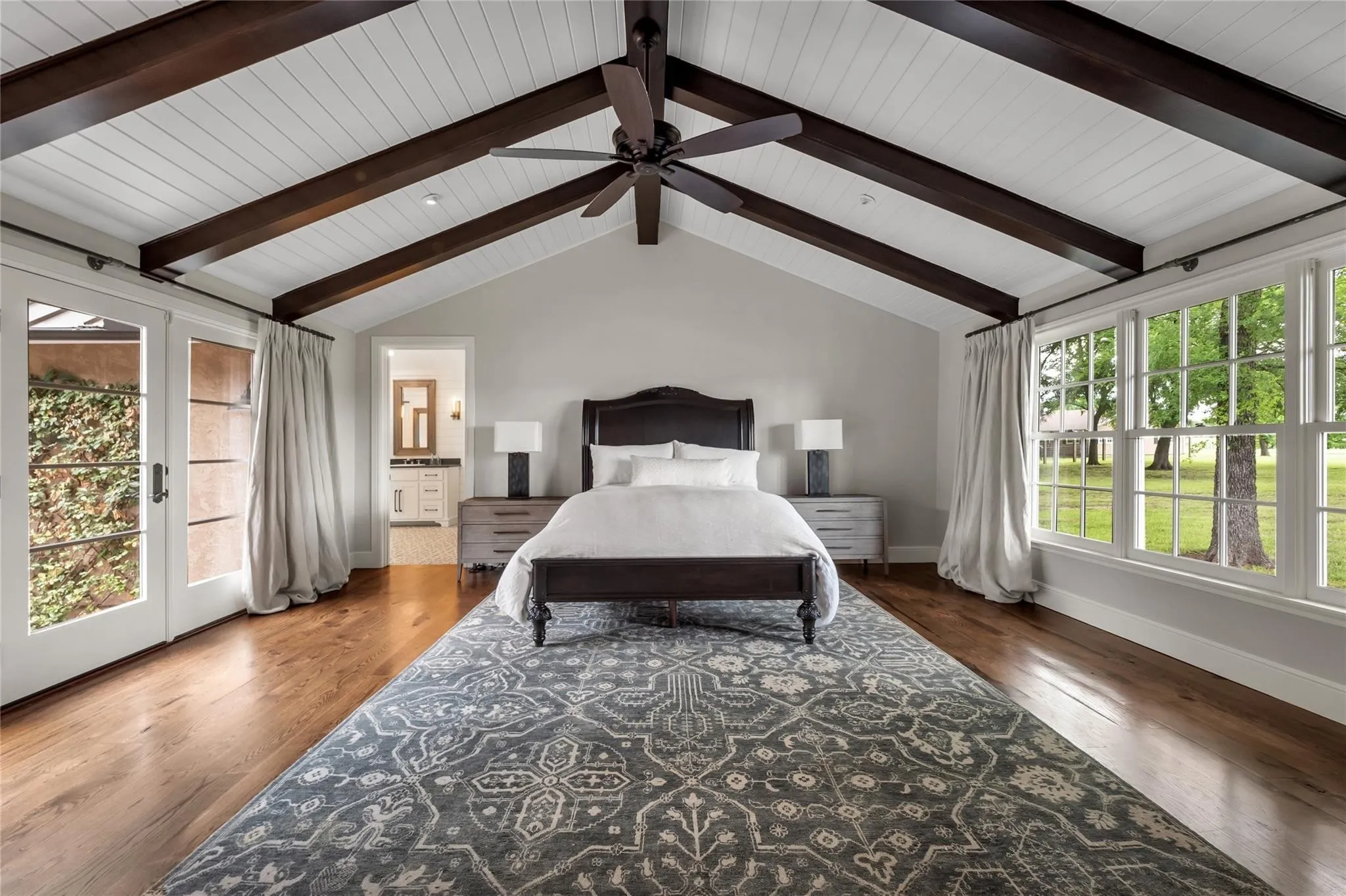 Vaulted ceiling with exposed wood beams, hardwood flooring, and large windows