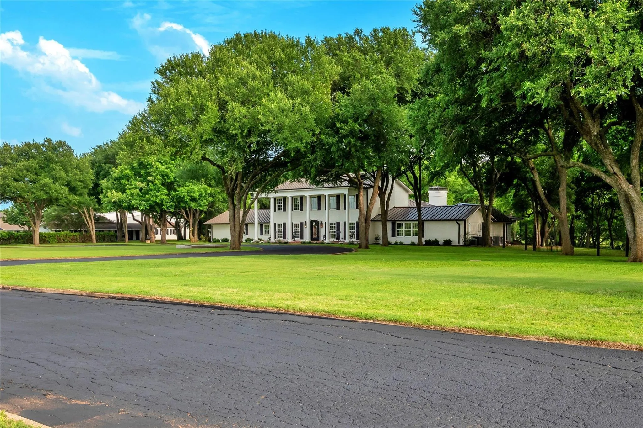 Expansive green lawn surrounds a classic white two-story residence with a columned portico