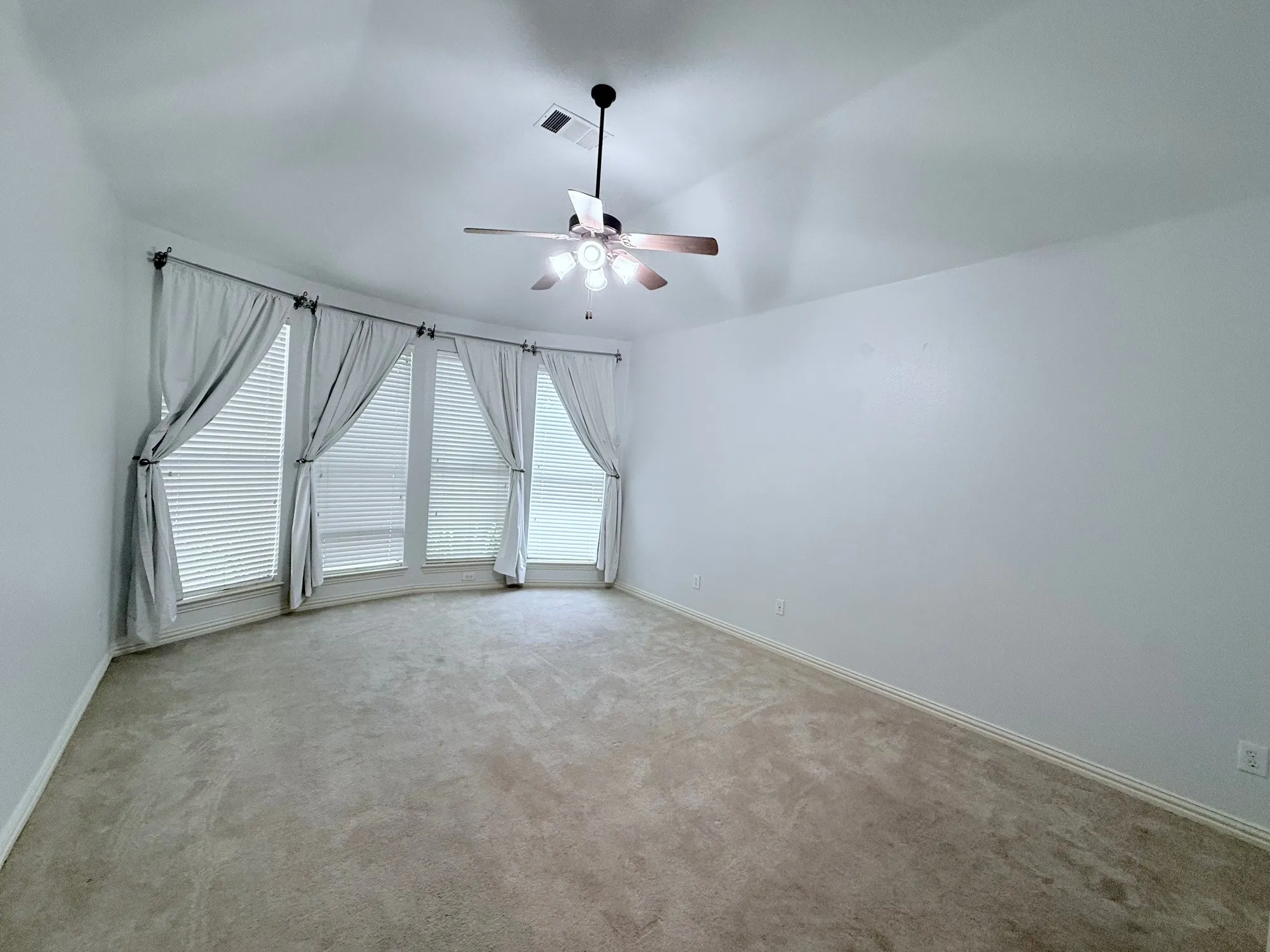 Bay window with multiple vertical blinds, neutral carpet, and ceiling fan with integrated lighting