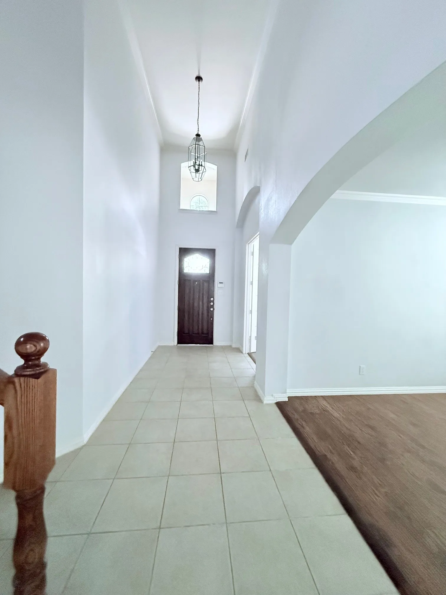 Two-story foyer with a decorative pendant light, transom window, tile flooring, and a dark wood-finish entry door