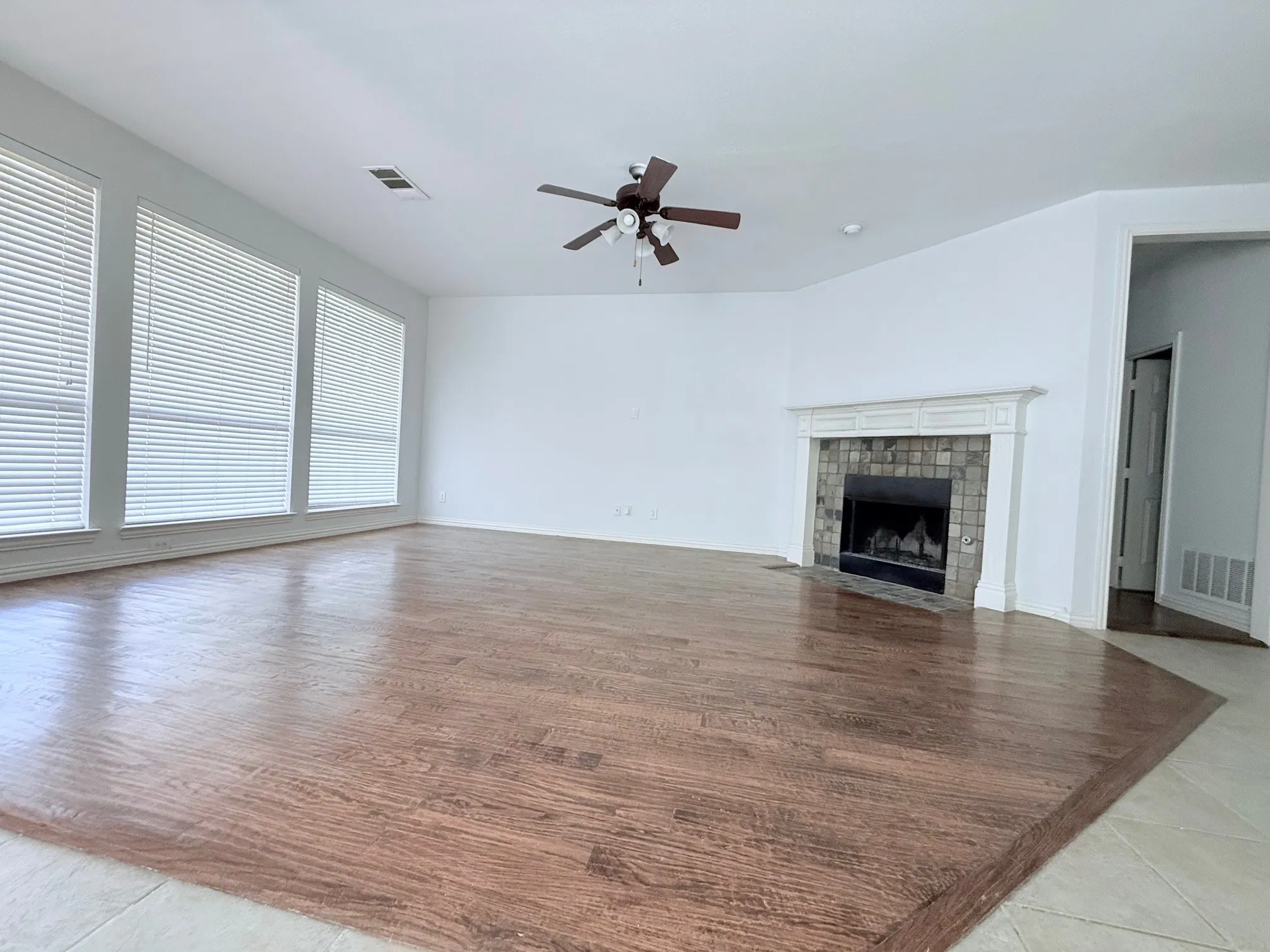 Expansive room featuring wood-finish flooring, a ceiling fan, and a fireplace with a decorative mantel and stone-tile surround