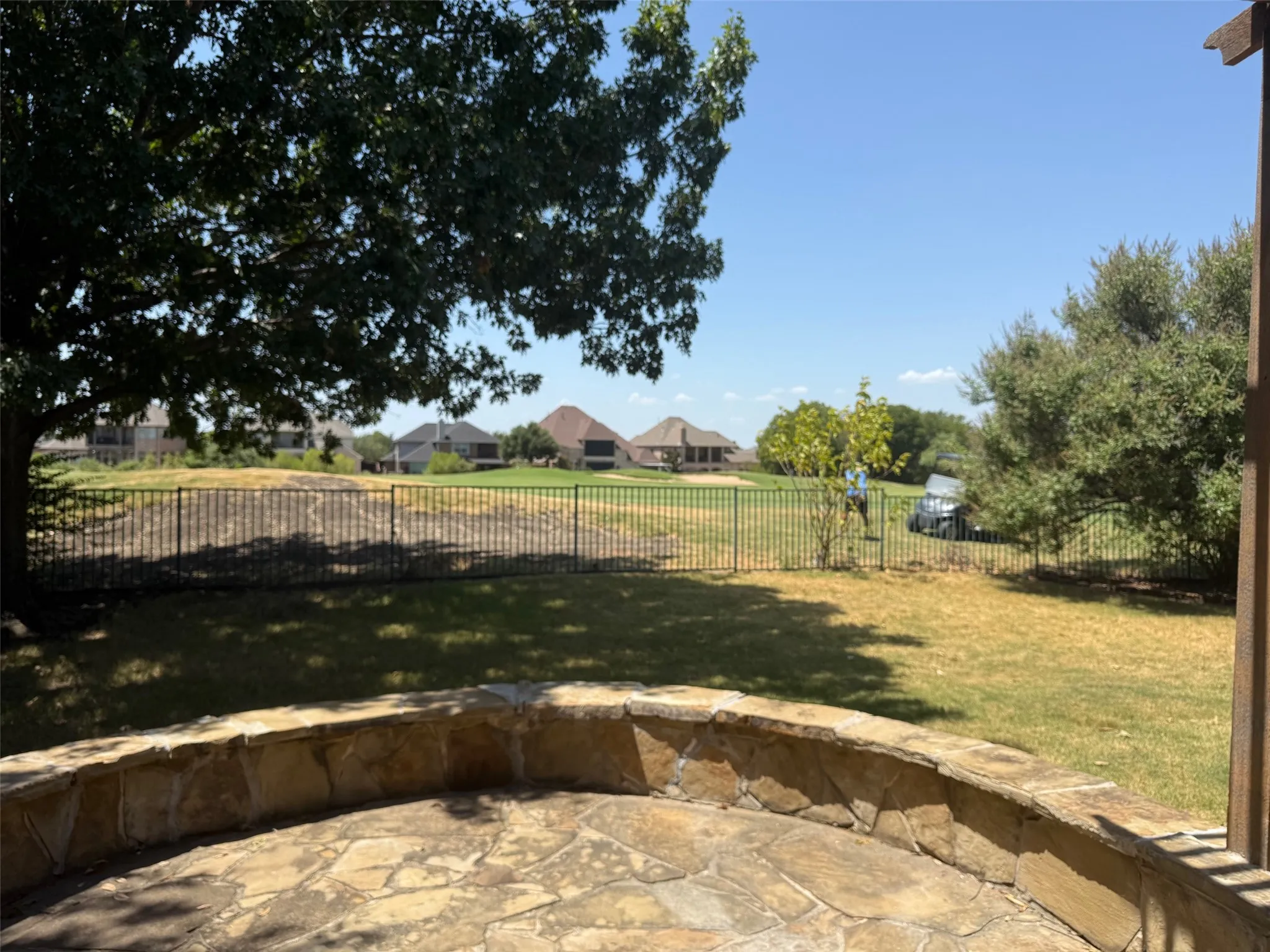 Curved flagstone patio with a stone retaining wall, fenced backyard, and mature trees