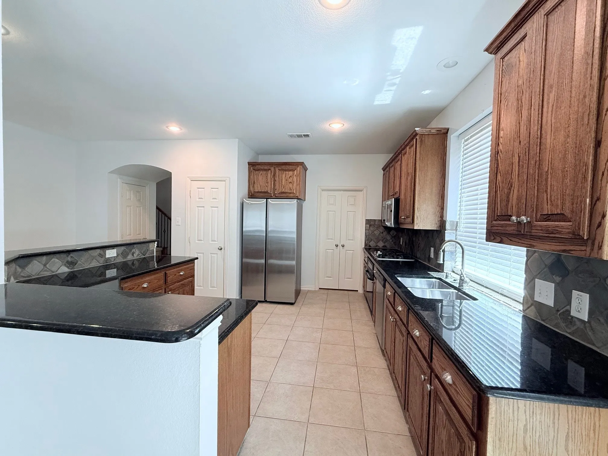 Kitchen featuring dark wood cabinetry, stainless steel appliances, black countertops, and a neutral tile backsplash