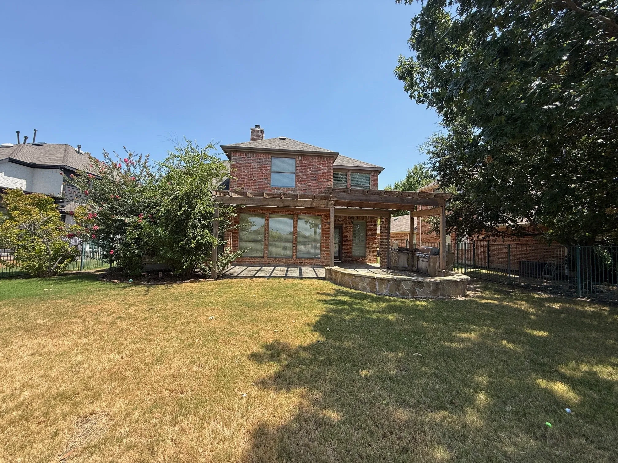 Brick exterior, ground-level patio, pergola, built-in stone outdoor kitchen, and fenced backyard