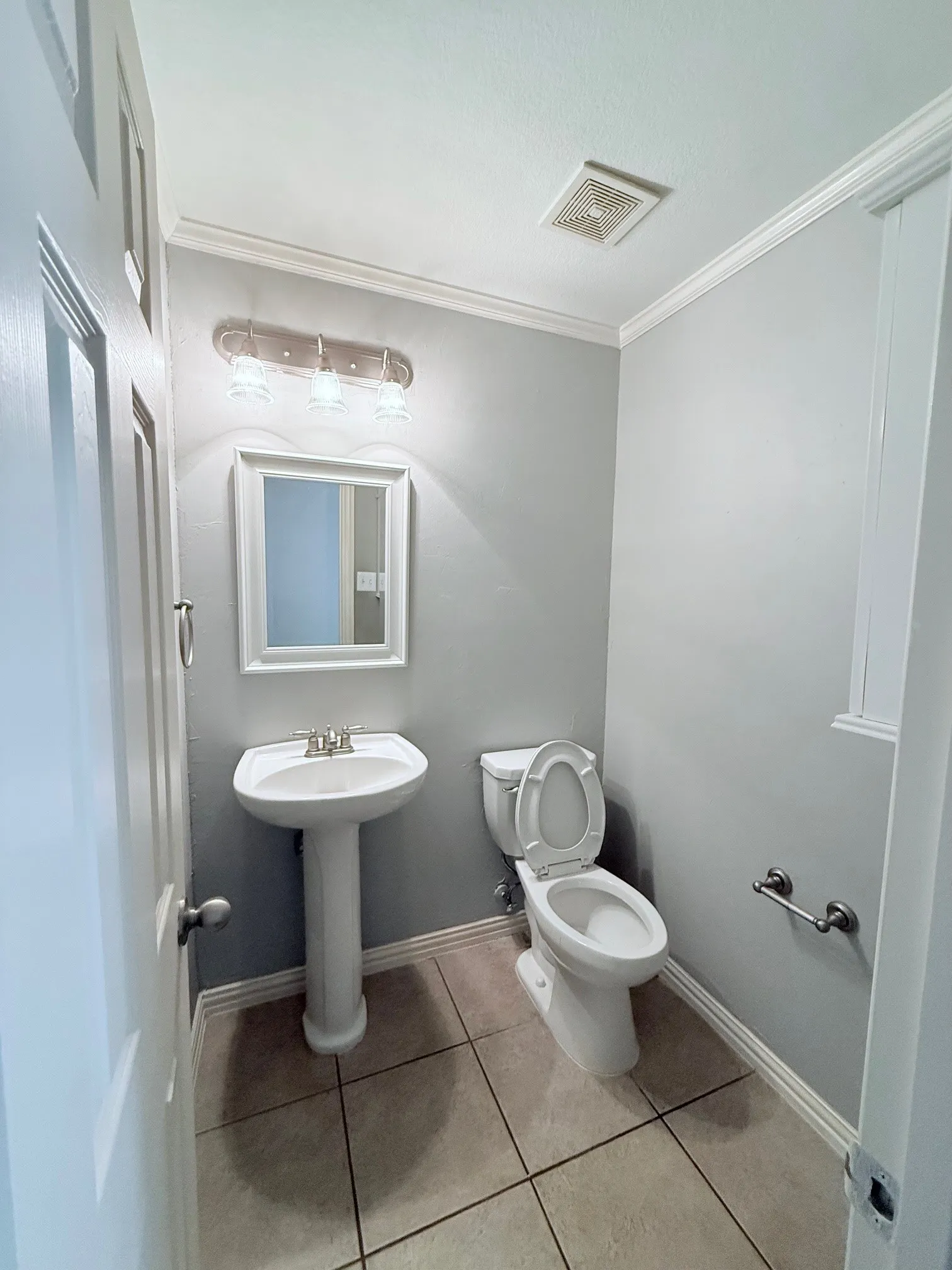 Pedestal sink with chrome faucet, ceramic toilet, tiled flooring, wall-mounted lighting fixture, and crown molding
