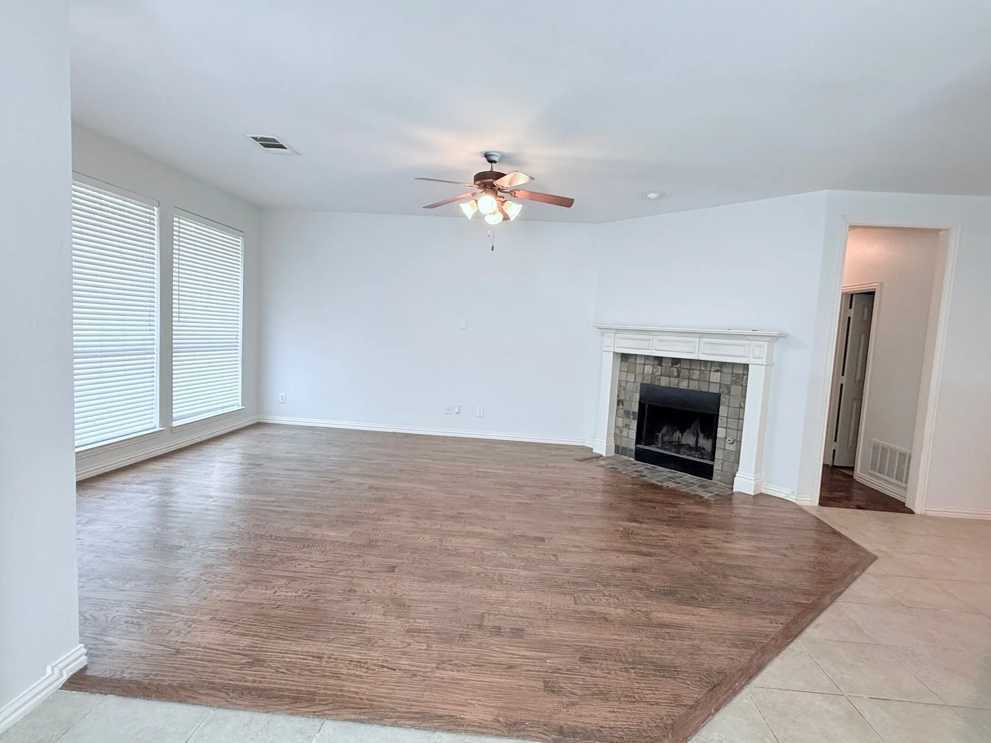 Spacious room with wood-finish flooring, a decorative fireplace with a stone surround, and multiple windows