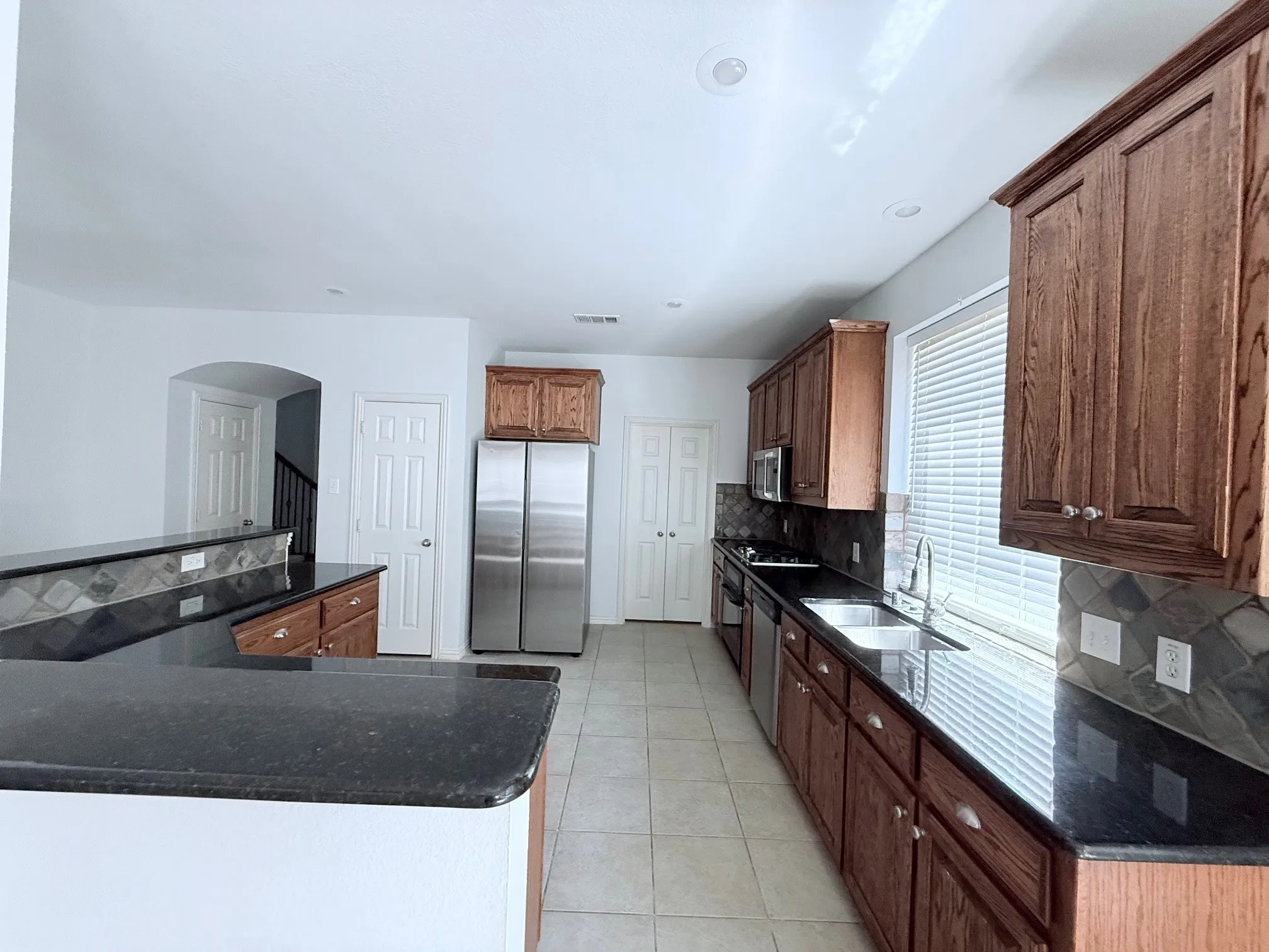 Kitchen featuring wood-finish cabinetry, dark countertops, stainless steel appliances, and tile flooring