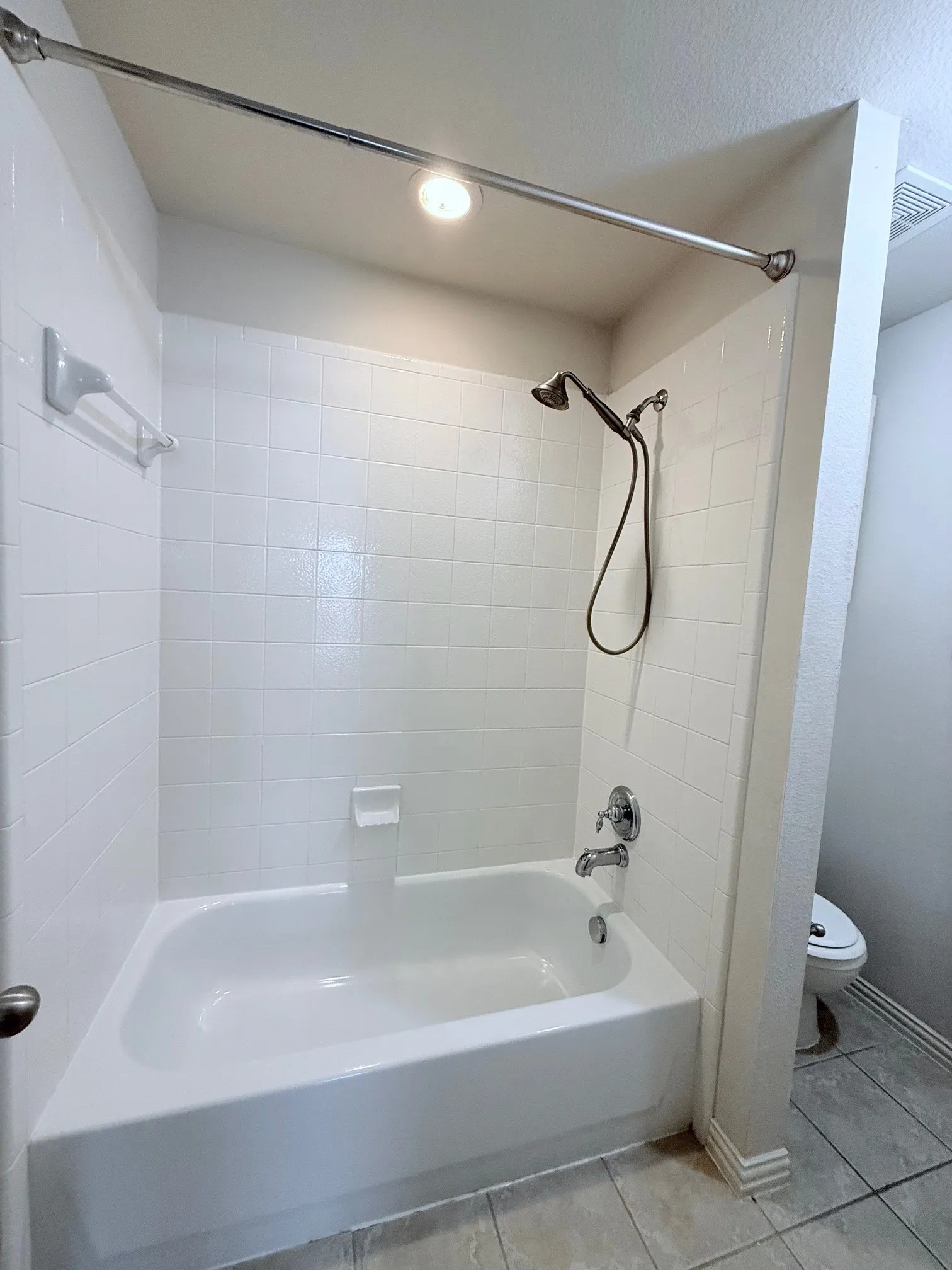 Bathtub with white subway tile surround, chrome fixtures, and an overhead showerhead