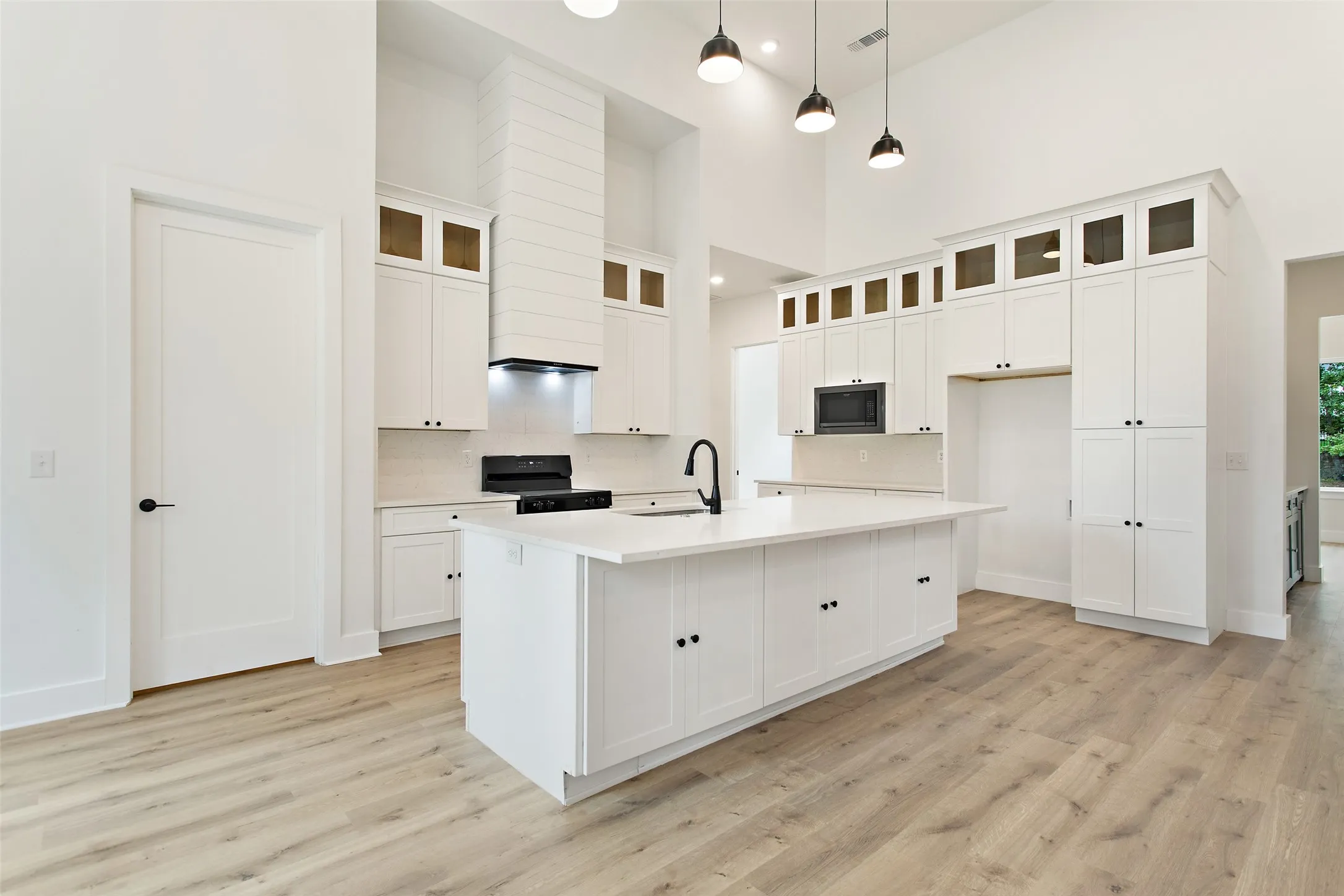 Vaulted ceilings, wood-finish flooring, white cabinetry with upper glass-front accents, and a large central island with an integrated sink