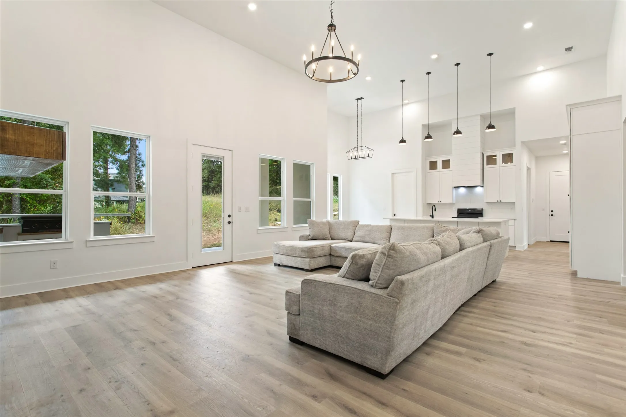 Soaring vaulted ceilings with recessed lighting, wood-finish flooring, and a modern kitchen featuring an island with pendant lighting and white cabinetry