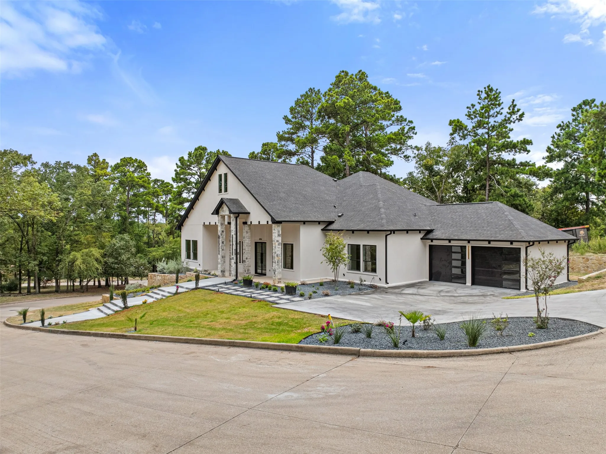 Contemporary architectural design with white stucco facade, stone column accents, dark trim, a two-car garage with frosted glass doors, and a landscaped front yard with a concrete driveway