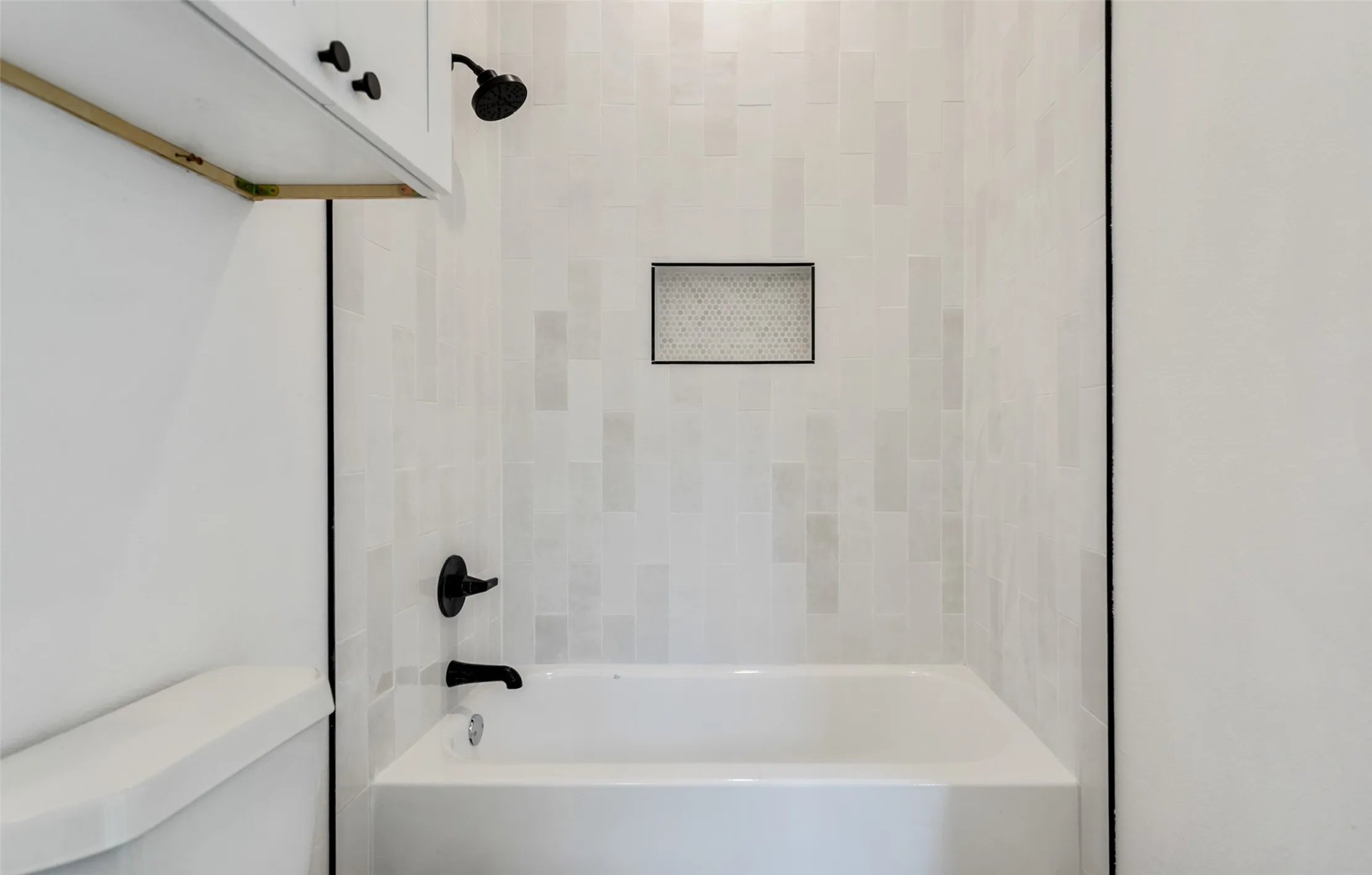 Bathtub with matte black fixtures, white subway tile surround, and a recessed shower niche