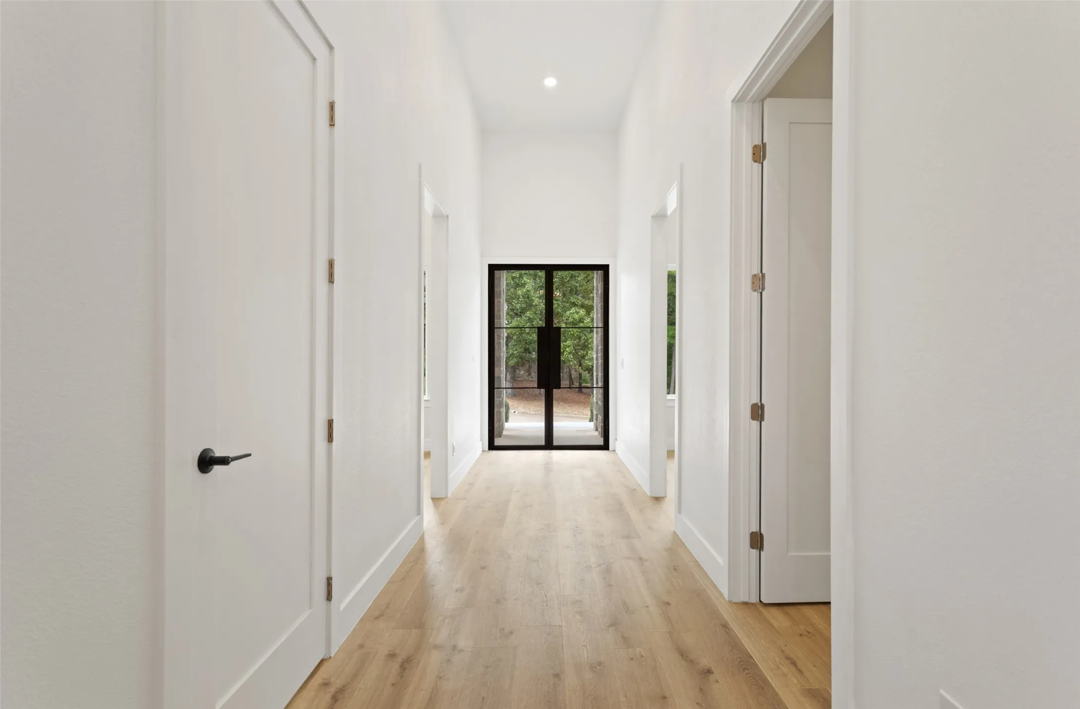 Hallway featuring wood-finish flooring, recessed lighting, white walls, and a black-framed glass​​‌​​​​‌​​‌‌​‌‌​​​‌‌​‌​‌​‌​​​‌​​ door