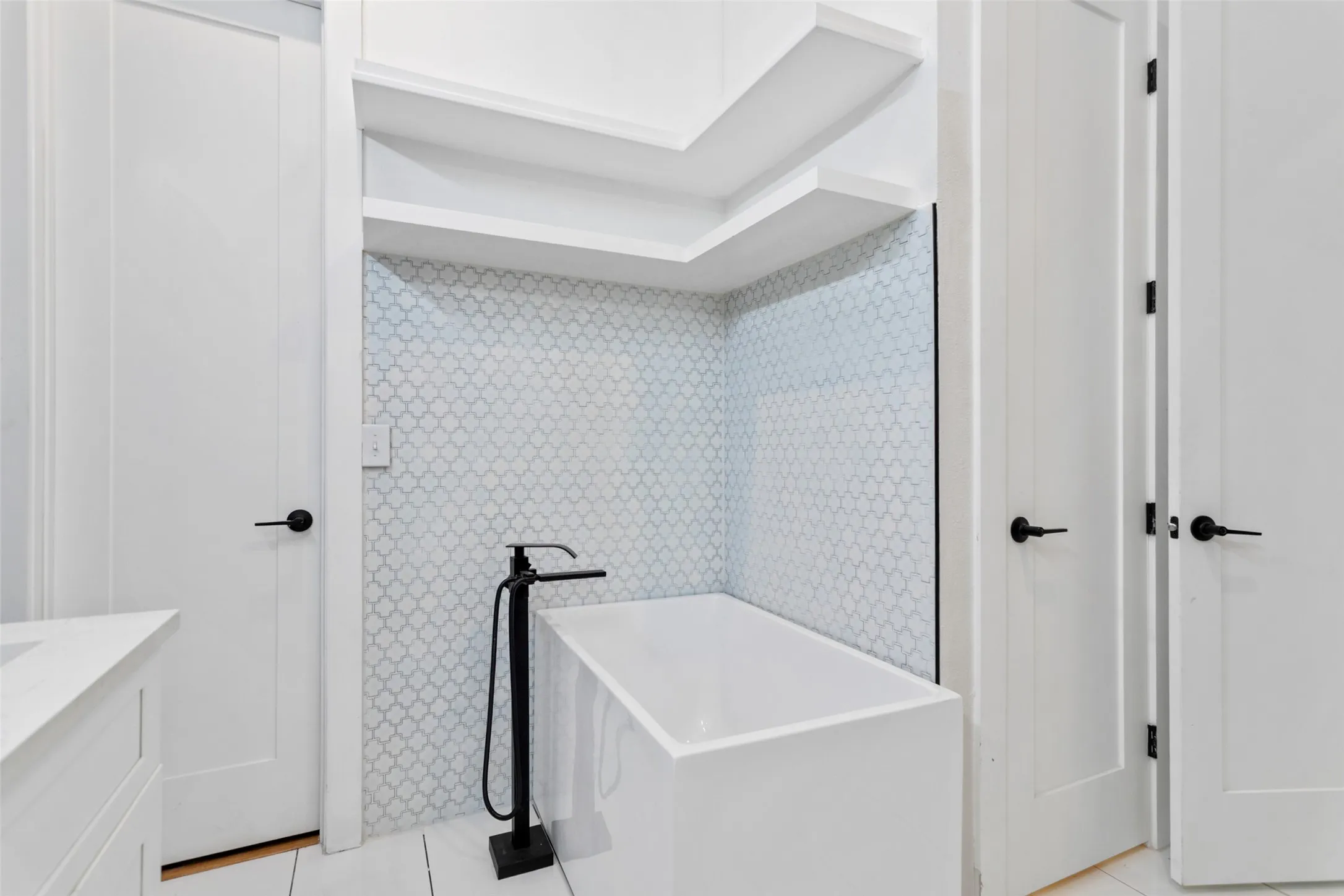 Freestanding soaking tub with a matte black floor-mounted faucet, alcove shelving, and patterned tile surround