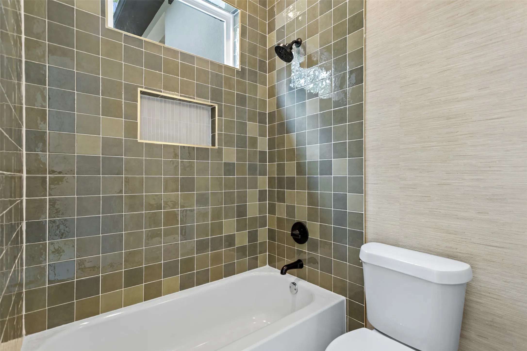 Subway tile tub surround with integrated shower niche, black finish shower fixtures, and a white porcelain tub