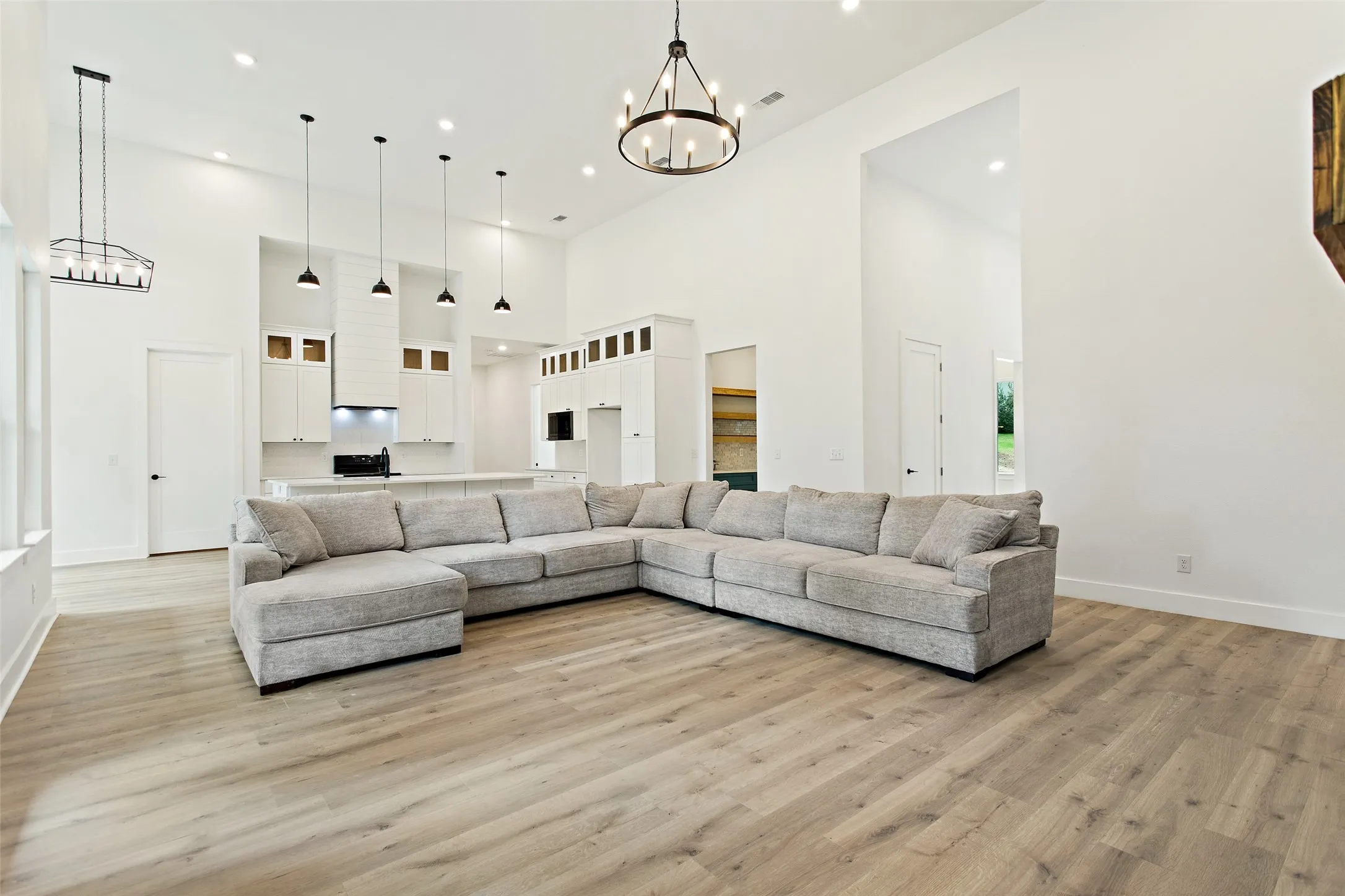Vaulted ceilings, wood-finish flooring, recessed lighting, and a kitchen featuring a range hood with pendant lights and white cabinetry