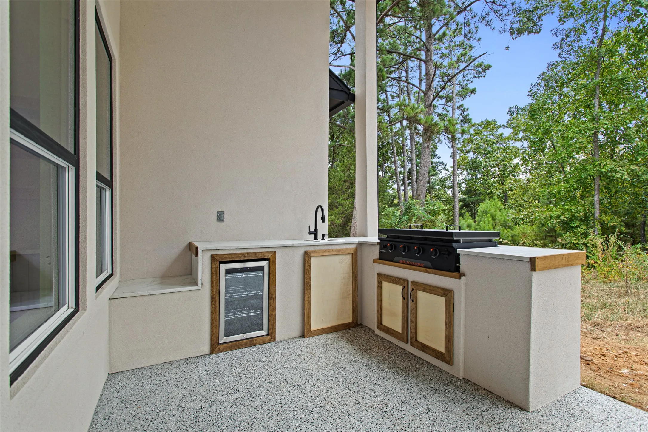 Outdoor kitchen featuring a built-in griddle, integrated beverage refrigerator, sink with matte black faucet, and wood-finish cabinetry