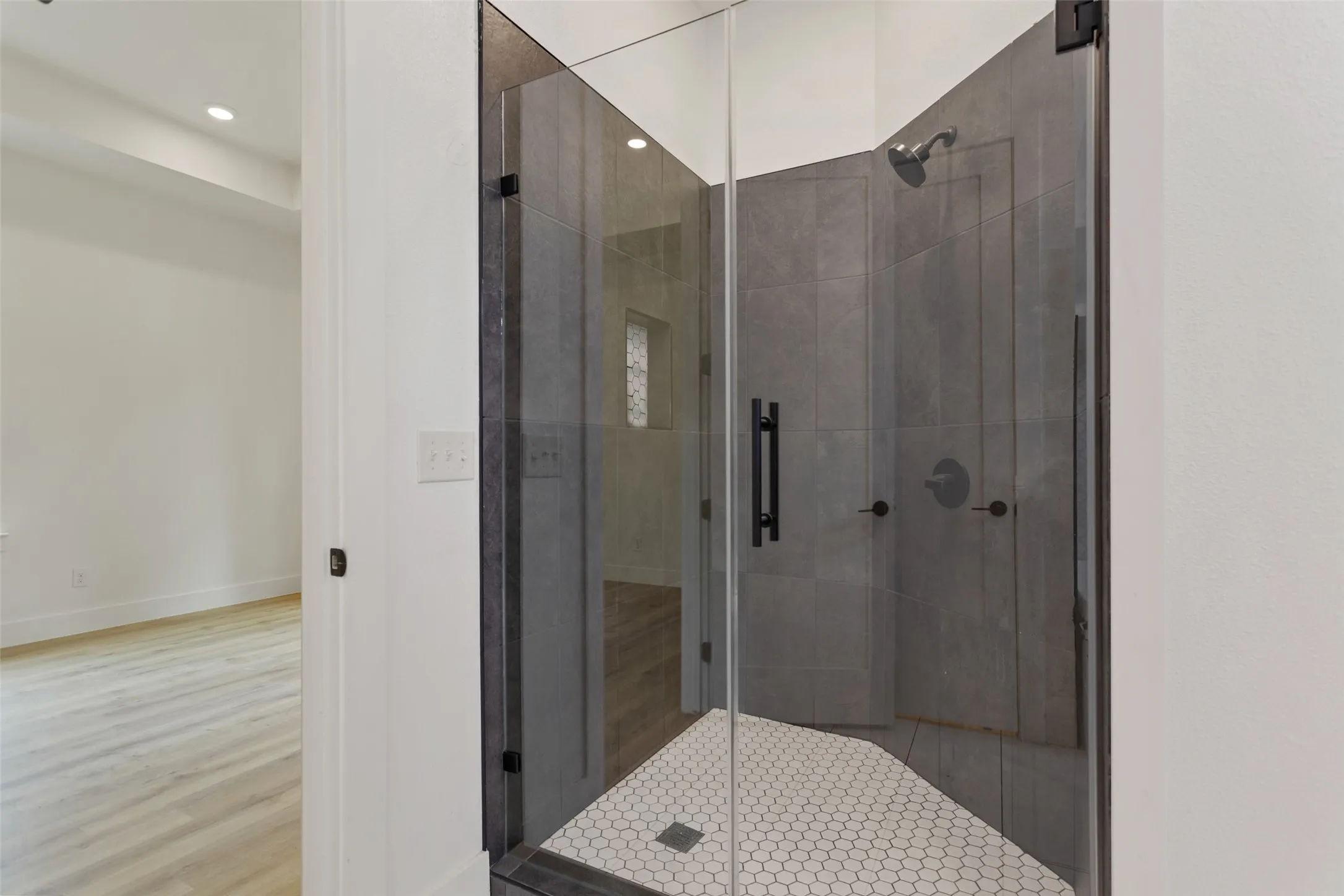 Glass-enclosed shower featuring large format wall tiles, a hexagon tile shower pan, and matte black fixtures