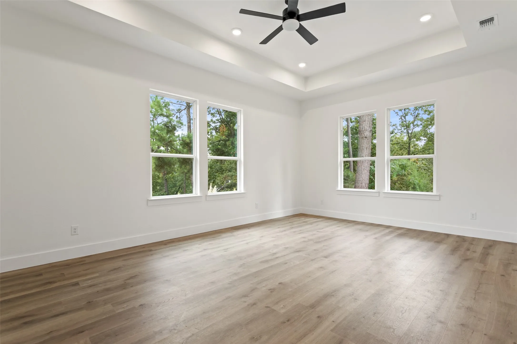 Tray ceiling featuring recessed lighting and a ceiling fan, complemented by wood-finish flooring and multiple windows