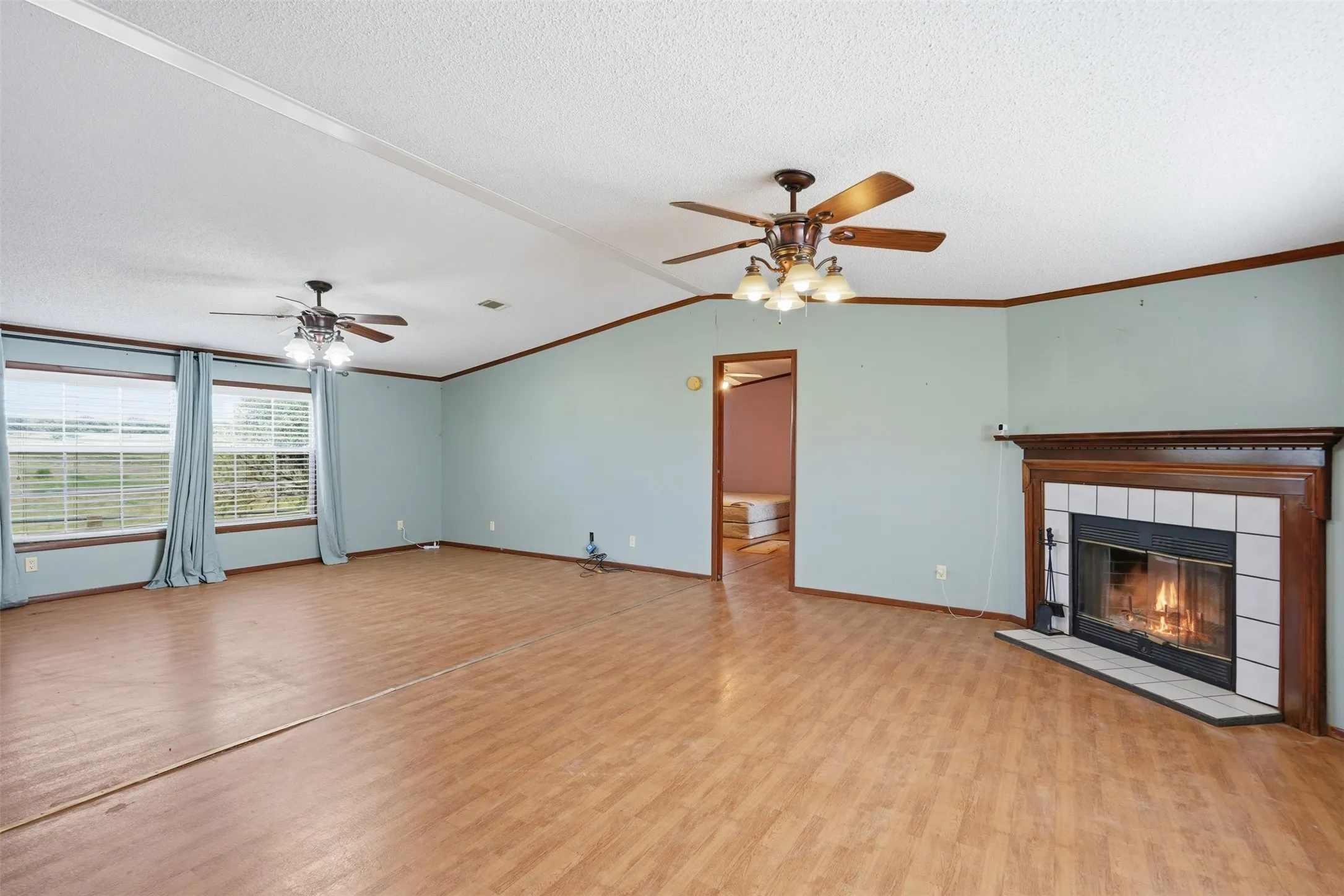 Expansive living space featuring wood-finish flooring, a tiled fireplace with wood mantle, and two ceiling fans