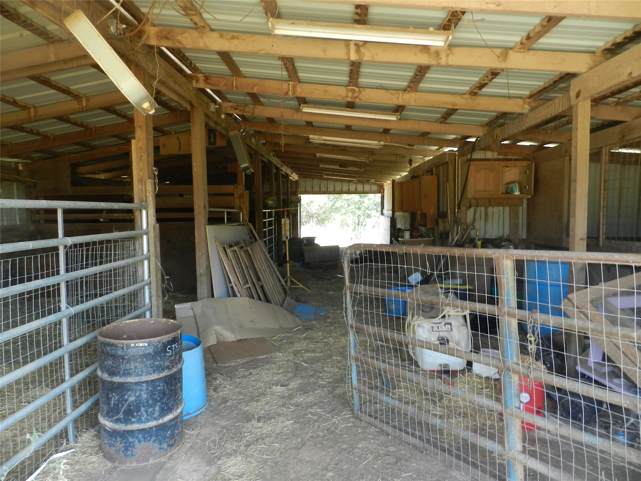 Enclosed barn structure with exposed wood beam ceiling, corrugated metal roof, and fluorescent lighting fixtures