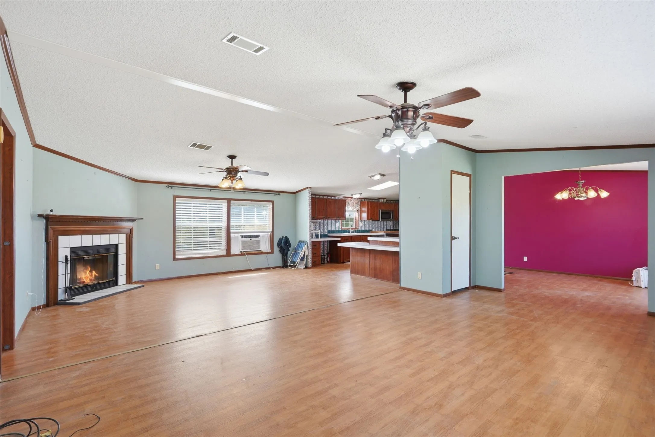 Expansive living area with wood-finish flooring, a fireplace with a white tile surround, multiple ceiling fans, and natural light from two windows