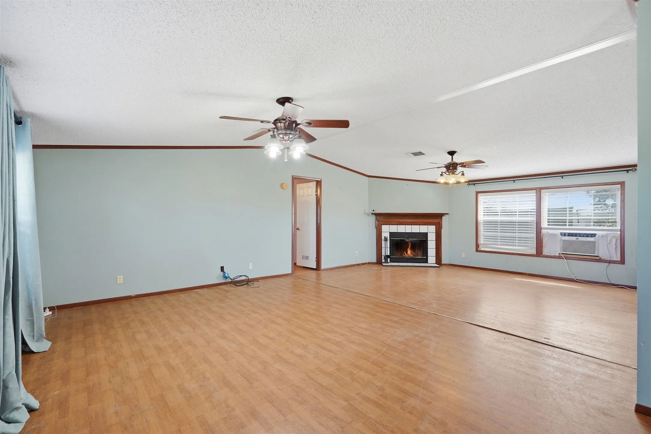 Spacious room with wood-finish flooring, a fireplace with a wood mantel, and multiple ceiling fans