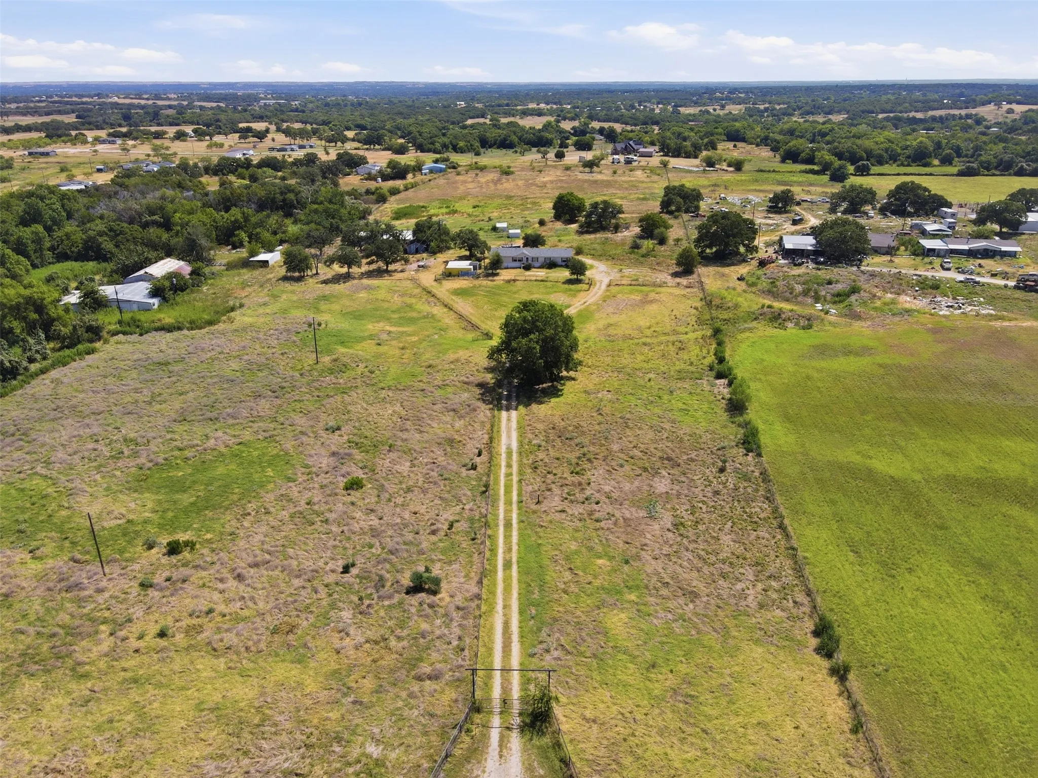 Expansive property featuring a long gravel driveway, mature trees, and a distant single-story residence