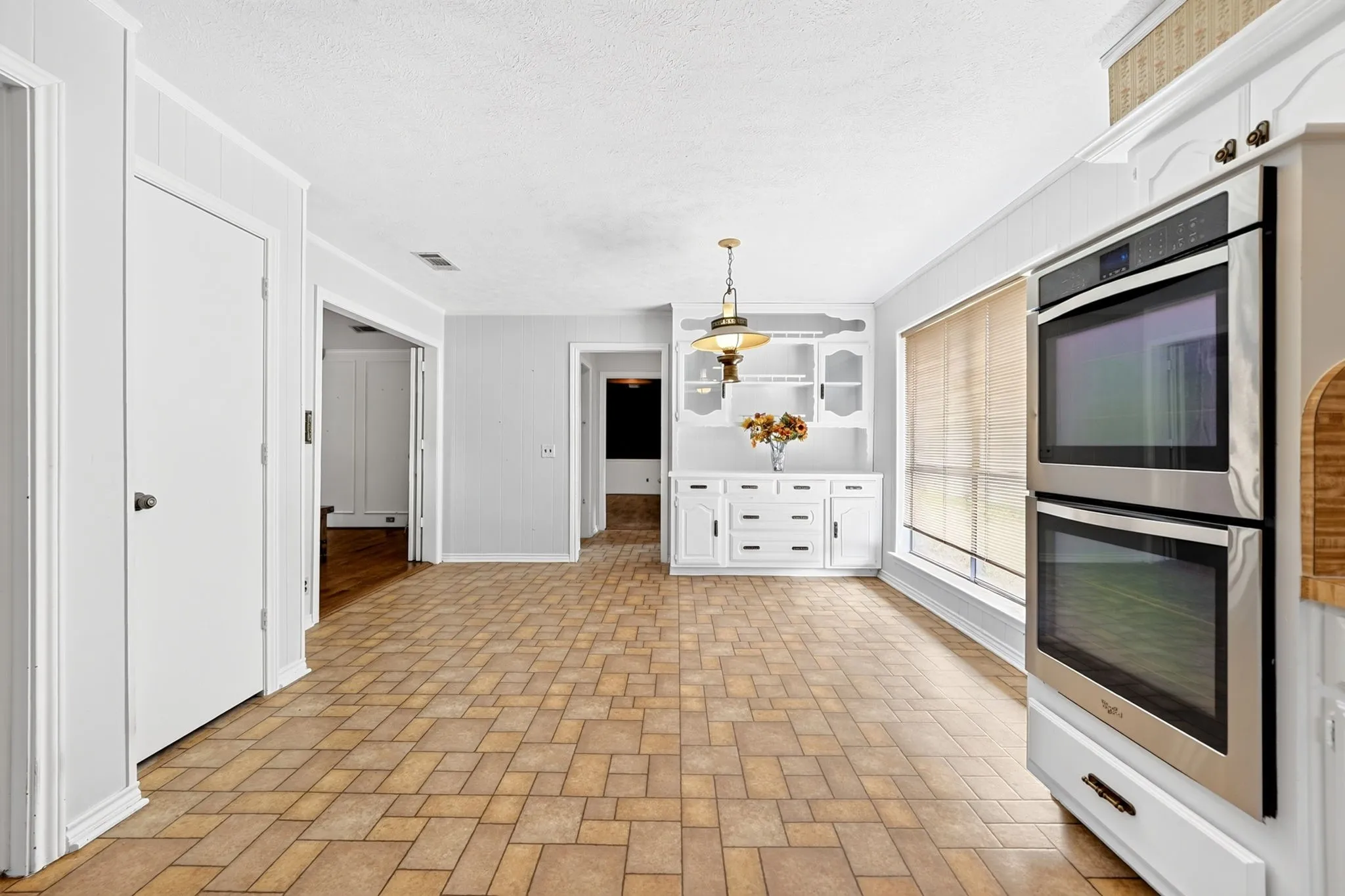 Spacious kitchen featuring wood-finish parquet flooring, dual wall-mounted stainless steel ovens, white cabinetry with integrated storage, and a central island with pendant lighting