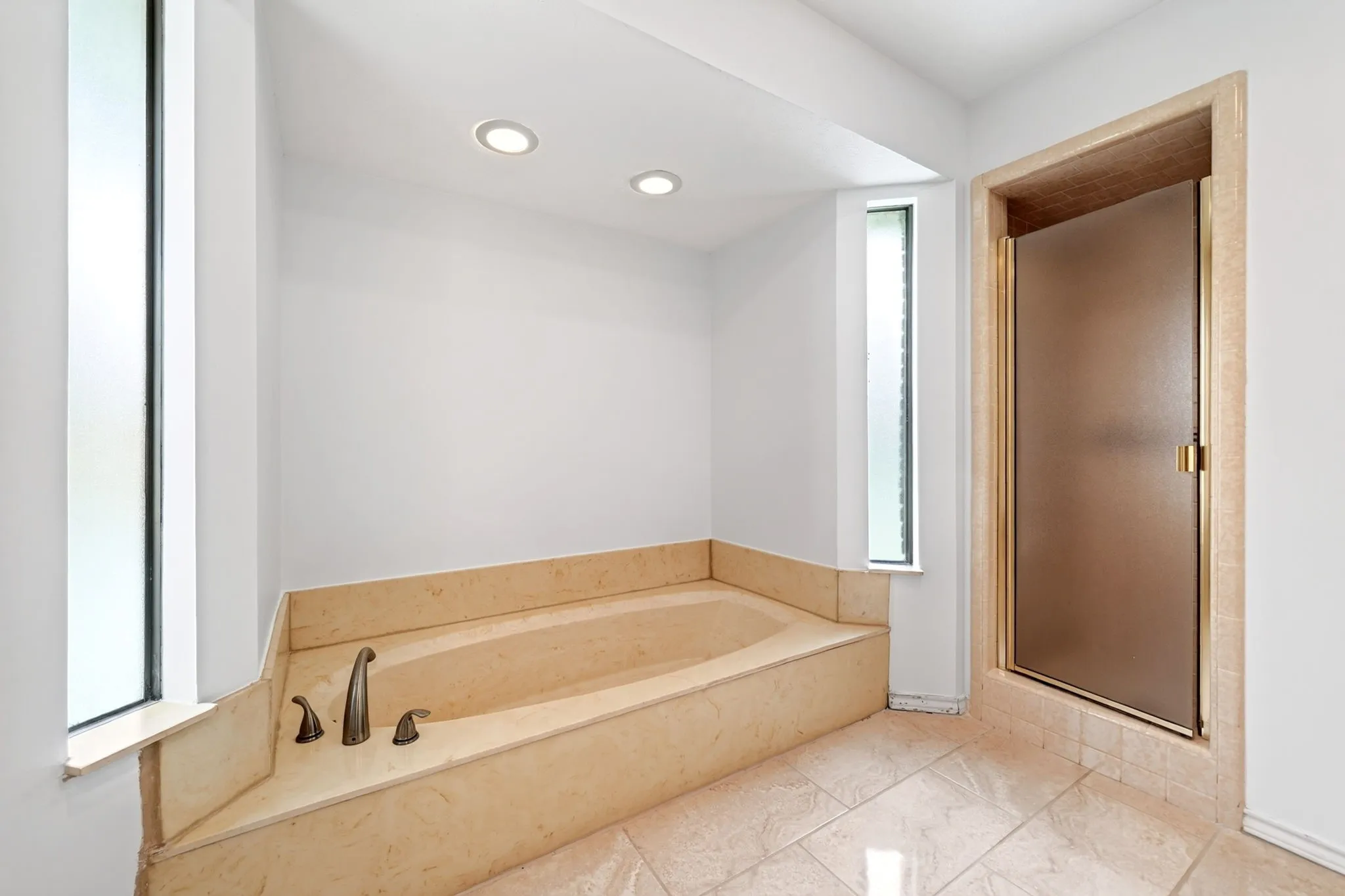 Recessed lighting, integrated soaking tub with dark bronze fixtures, frosted privacy windows, and a tiled shower enclosure with a frosted glass door
