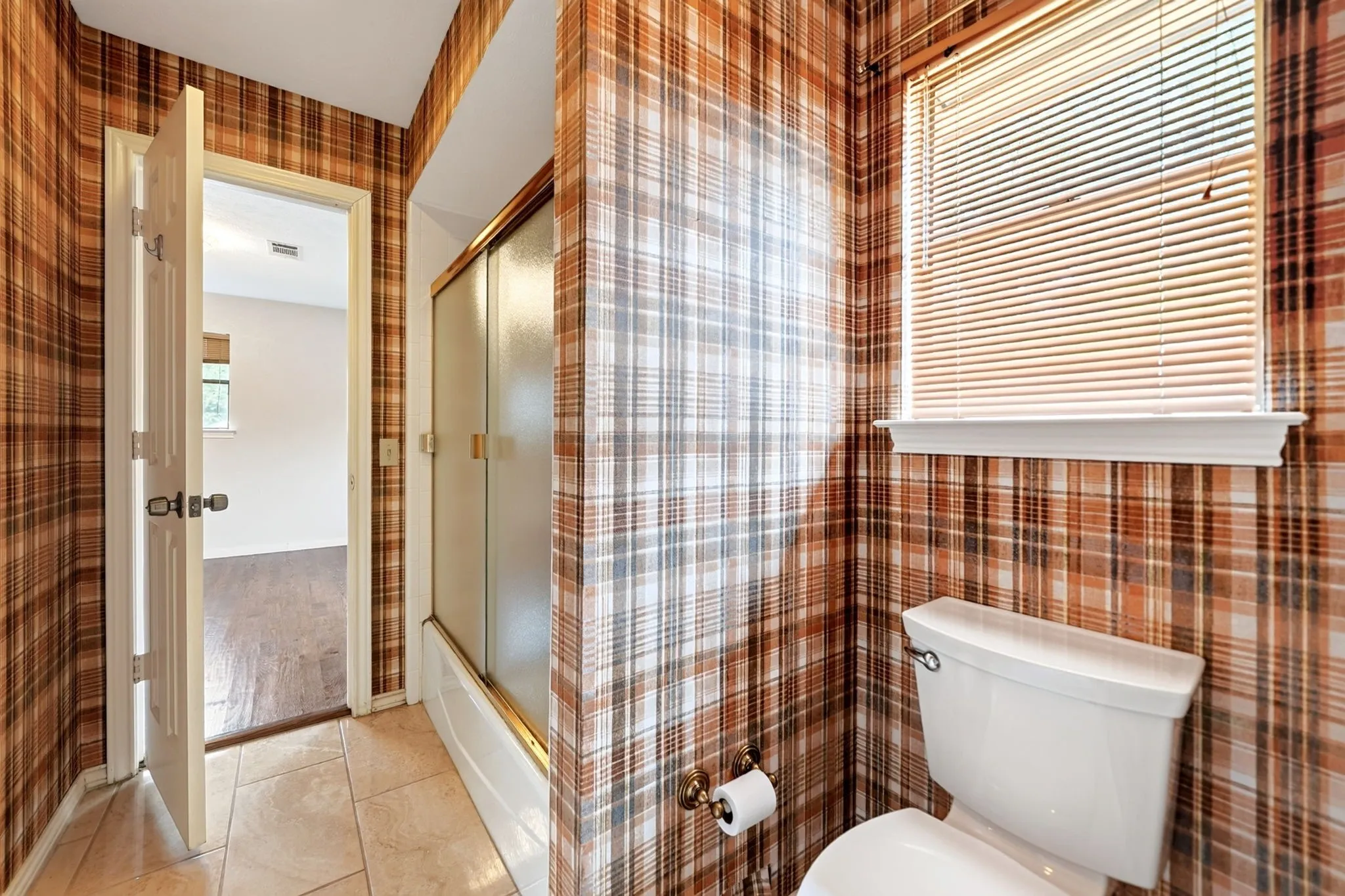 Tiled flooring, built-in tub with glass shower enclosure, and a window with blinds