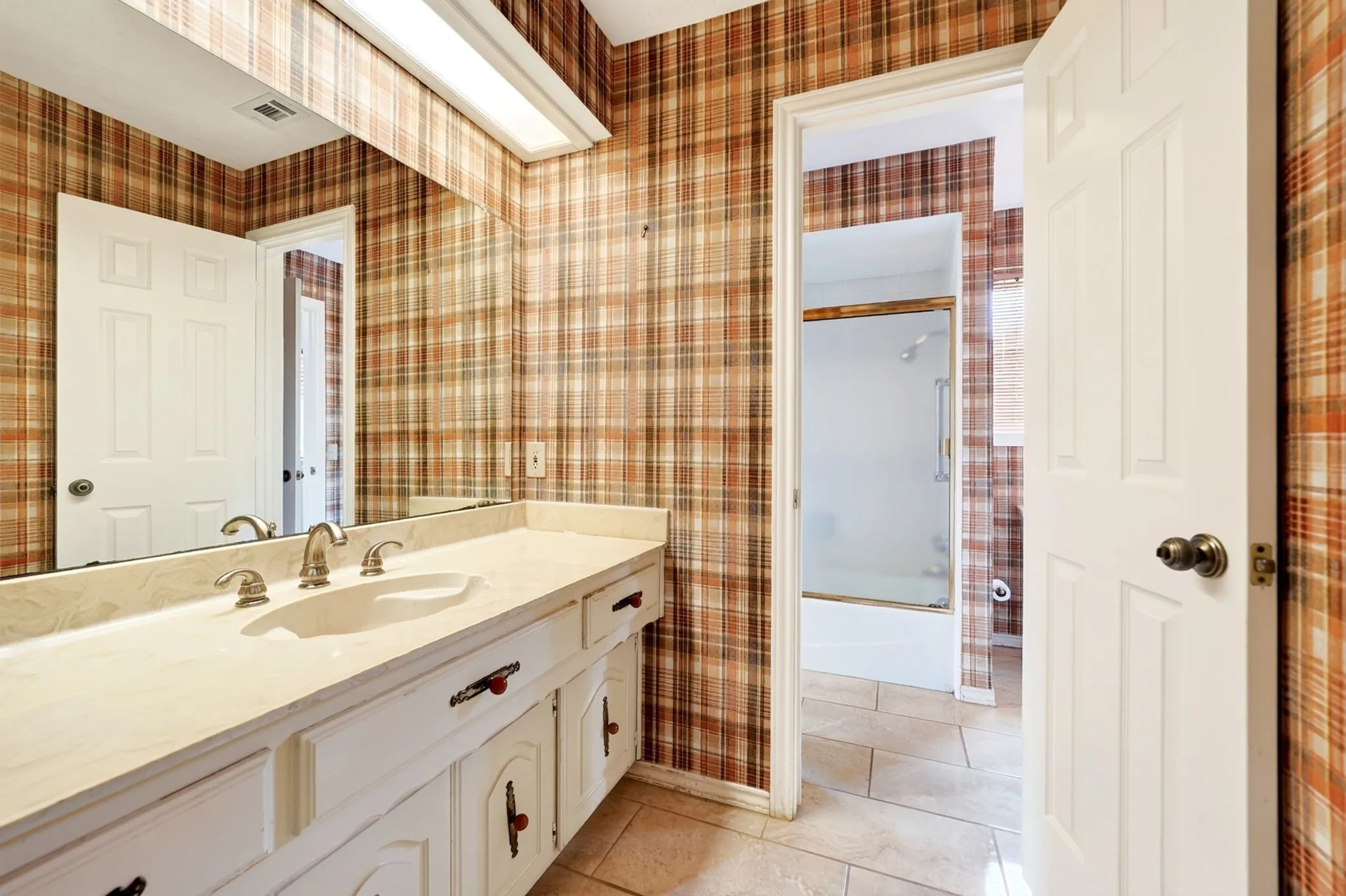 Master bathroom featuring dual vanity with cream cabinetry, brushed nickel fixtures, and an expansive mirror