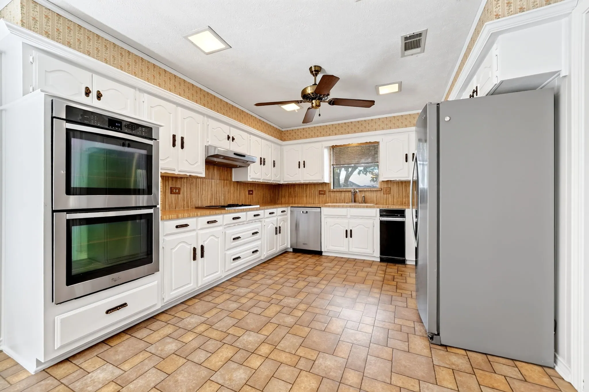 Kitchen featuring white cabinetry, tile flooring, stainless steel double wall ovens, a built-in dishwasher, and a ceiling fan