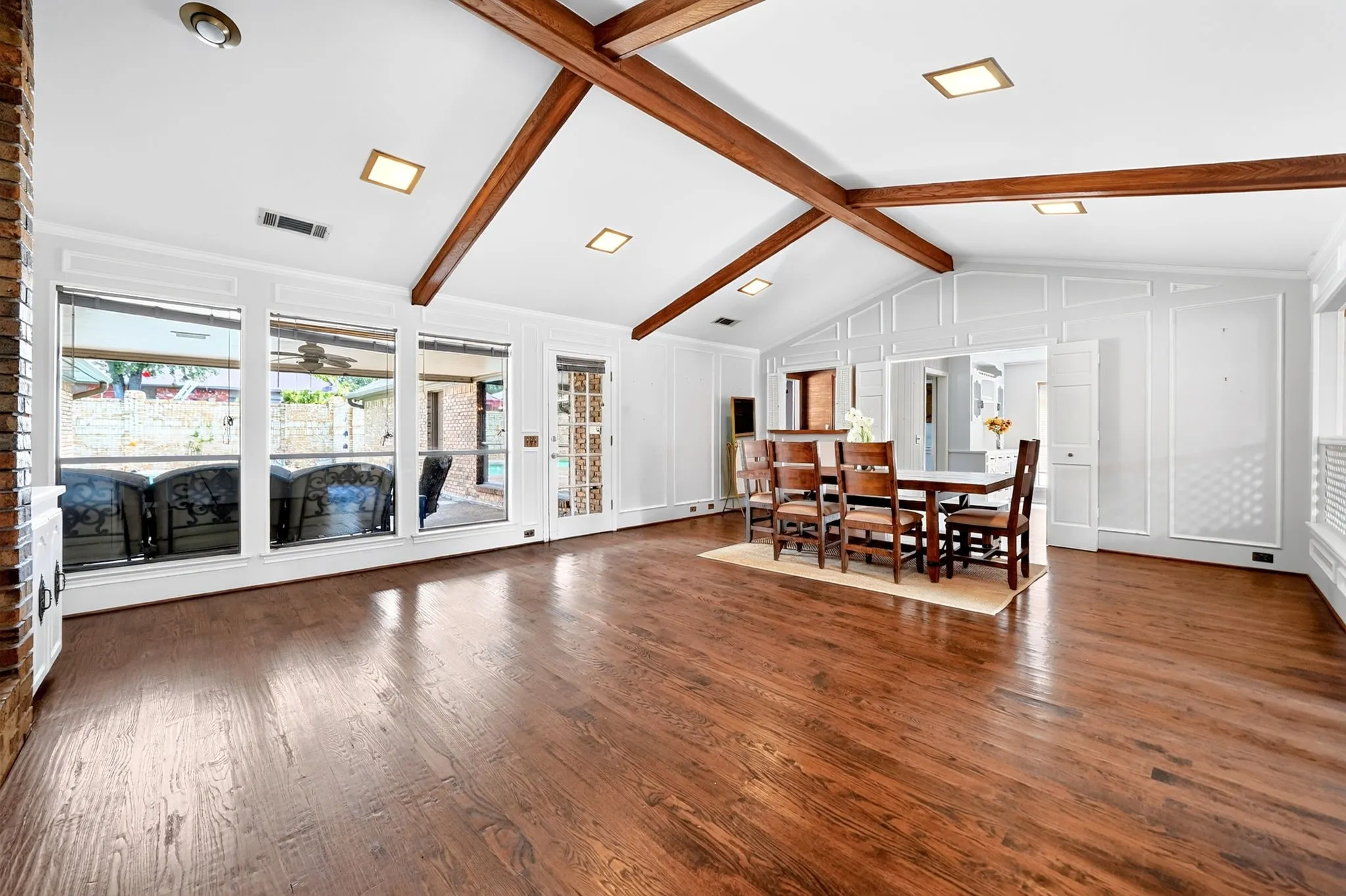 Vaulted ceiling with exposed wood beams, hardwood flooring, full-length windows, and wainscoting