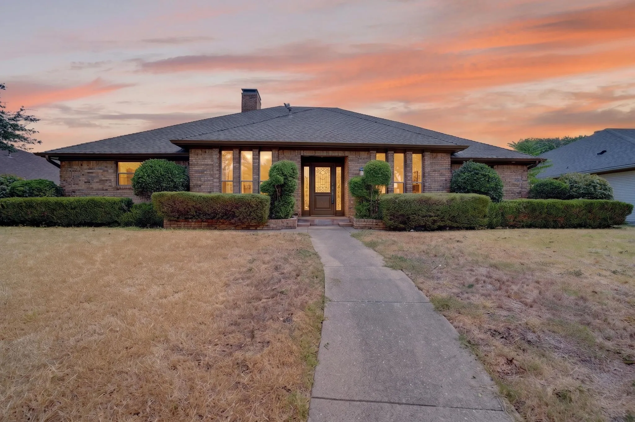 Contemporary brick residence showcasing a low-pitched roofline, symmetrical façade with multiple tall windows featuring warm interior lighting, and a centered entry portico